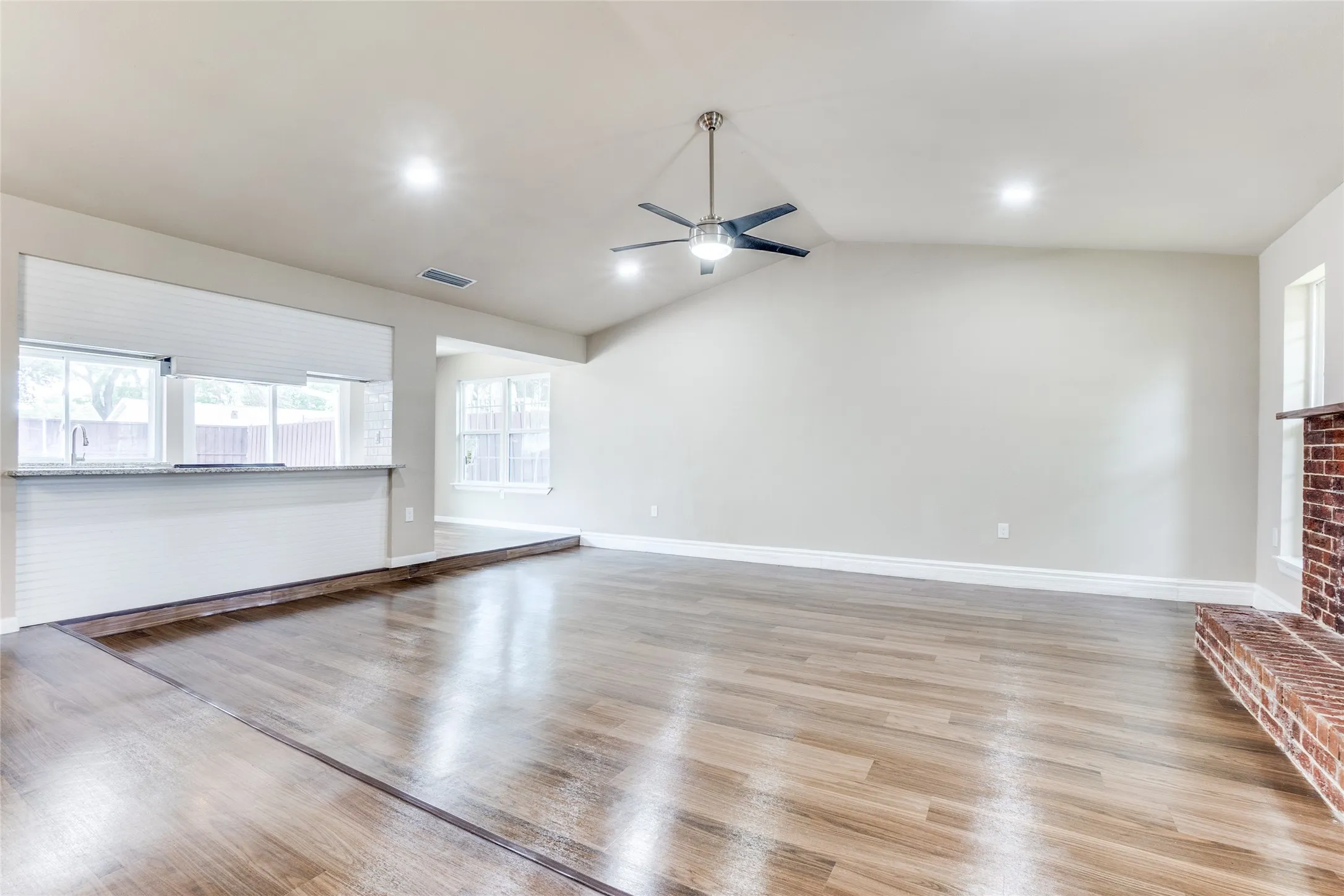 Vaulted ceiling, wood-finish flooring, recessed lighting, ceiling fan, and a brick fireplace