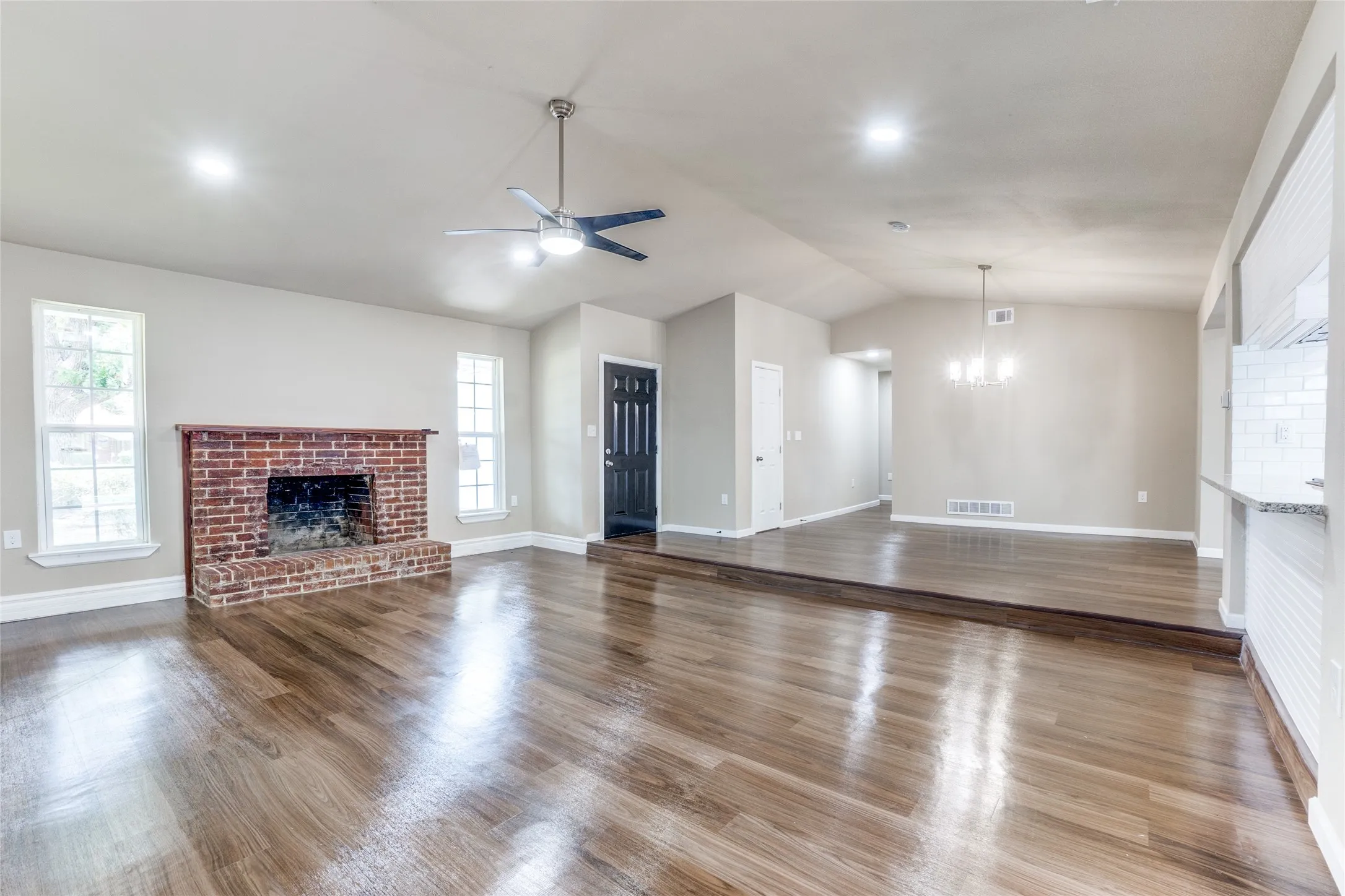 Wood-finish flooring, brick fireplace, vaulted ceilings, recessed lighting, and a modern ceiling fan