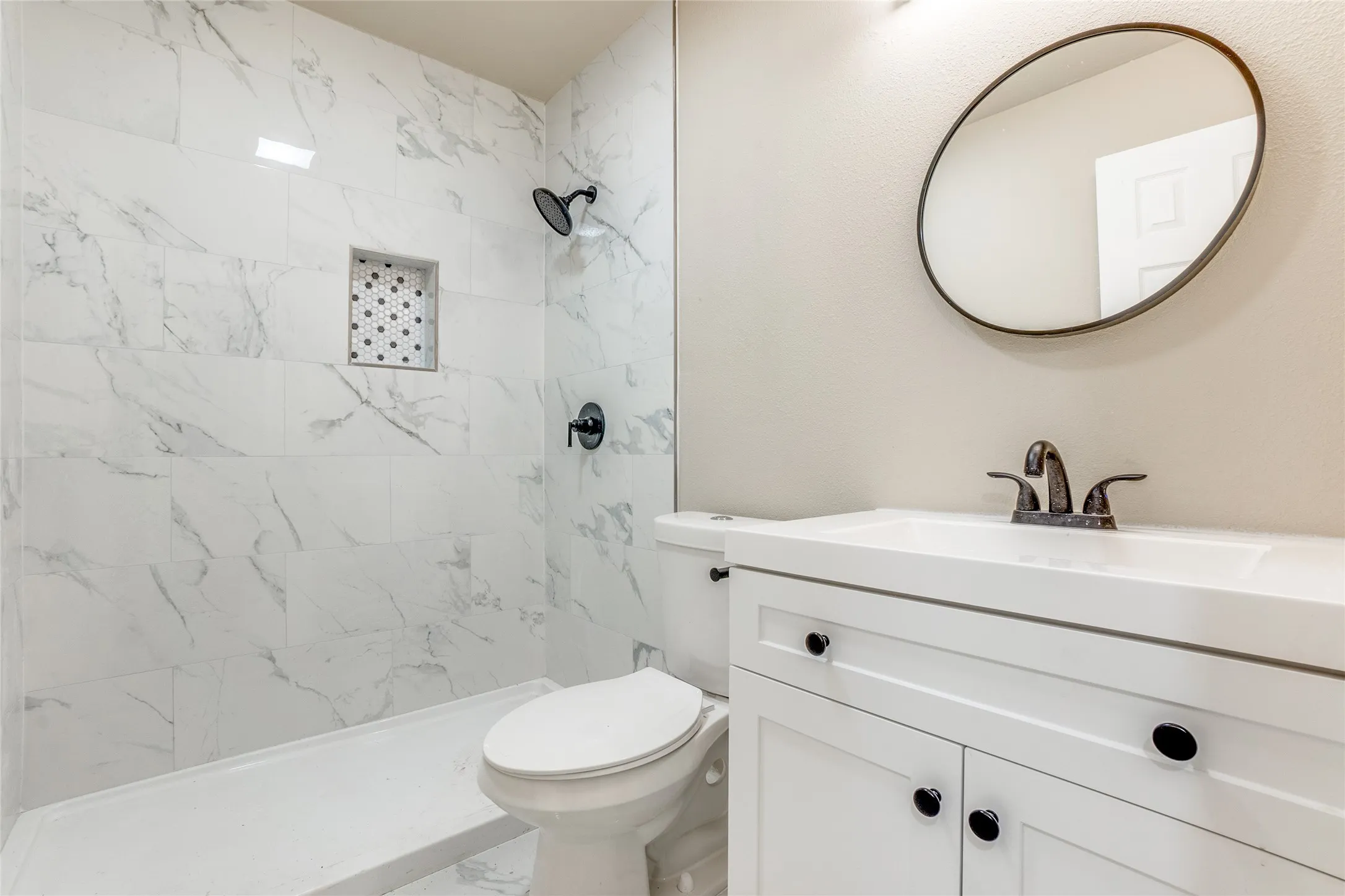 White vanity with integrated sink, black hardware, and an oval mirror