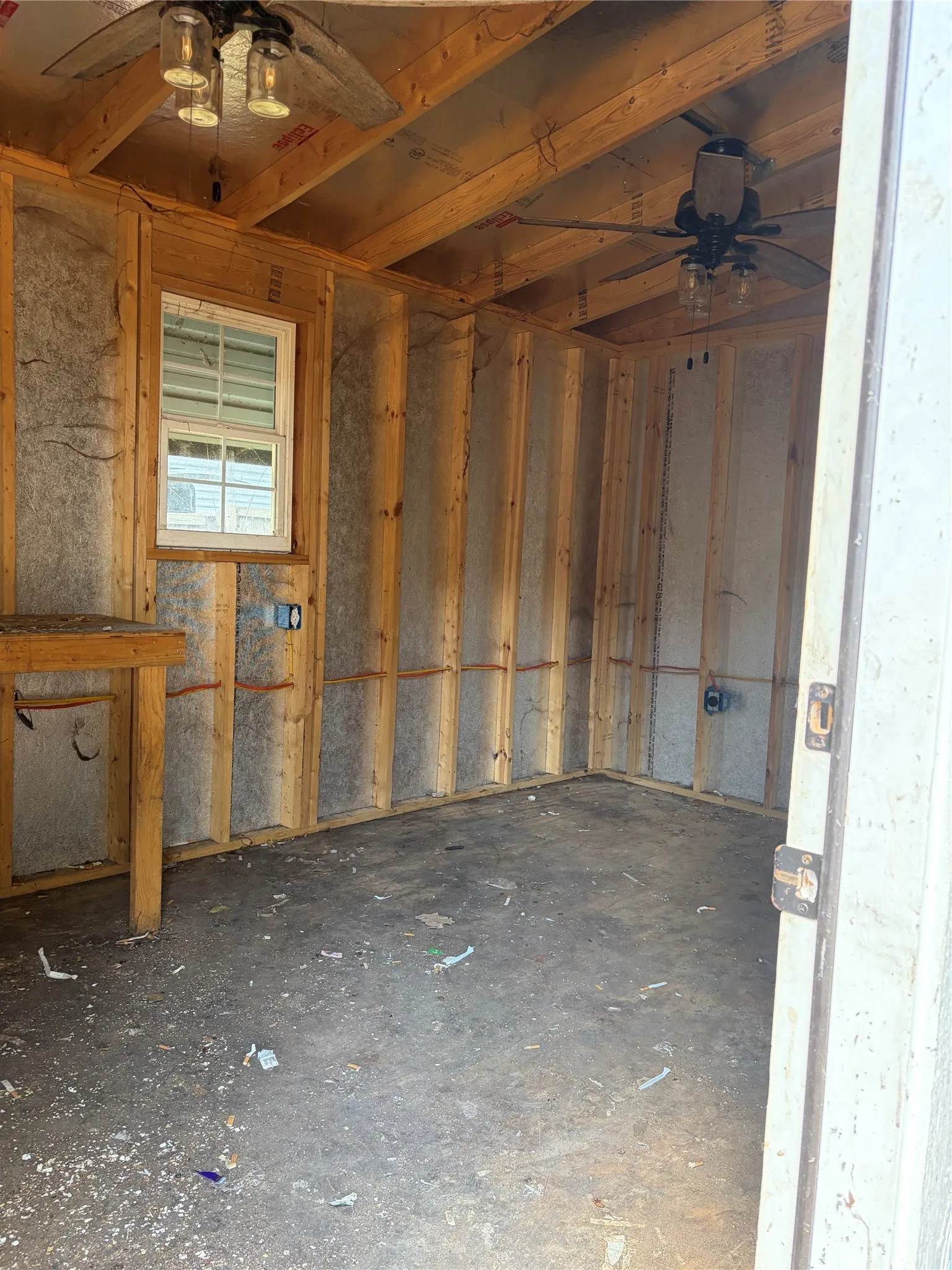 Exposed wood framing, dual ceiling fans with integrated lighting, built-in window, and a concrete floor