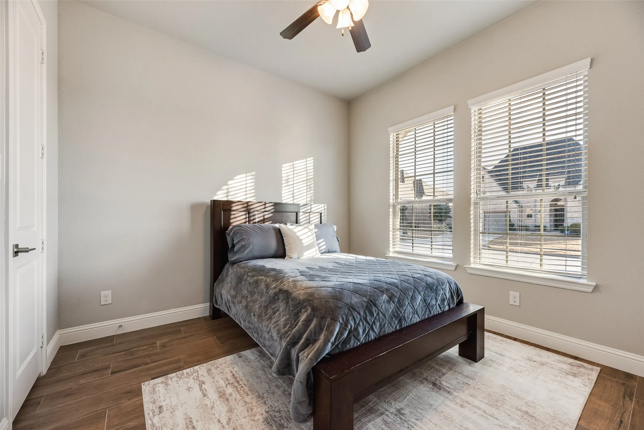 Wood-finish flooring, two large windows with blinds, ceiling fan with integrated lighting, and a paneled interior door