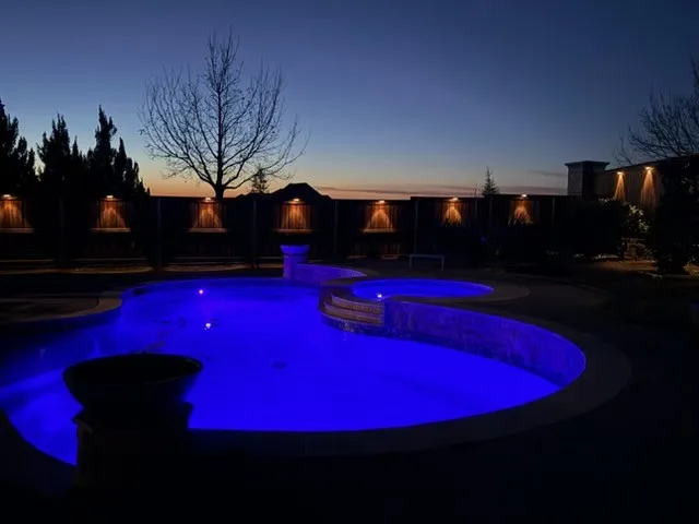 Freeform pool with integrated spa, illuminated water features, and perimeter accent lighting