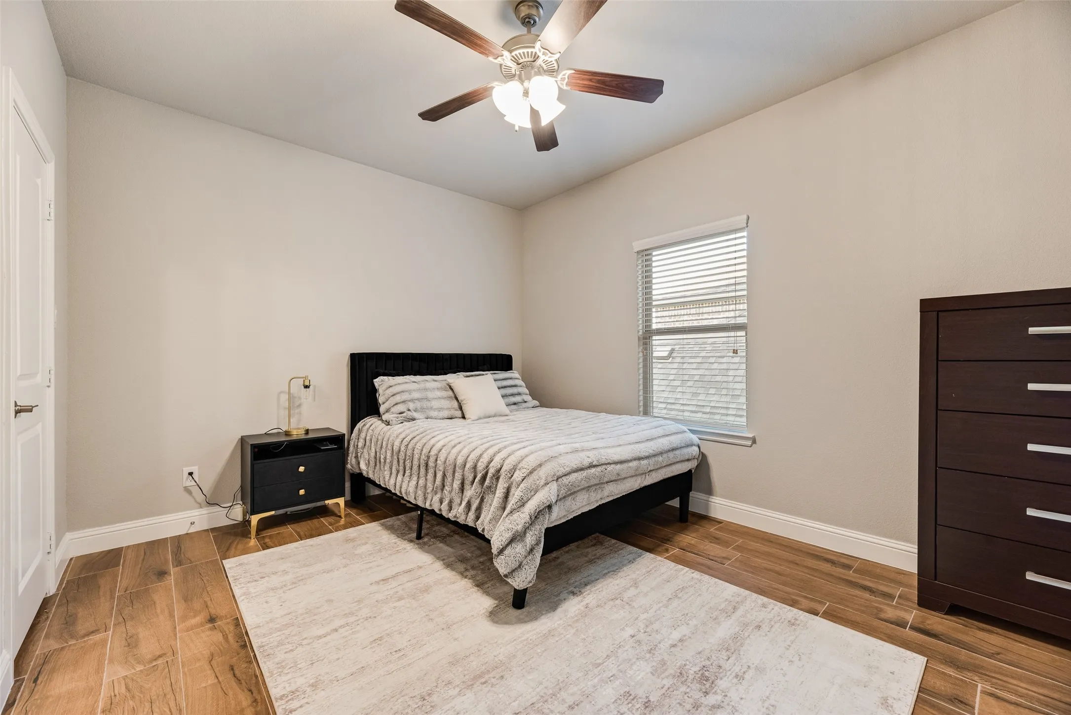 Room featuring wood-look tile flooring, light-toned walls, a window with blinds, and a ceiling fan with integrated lighting