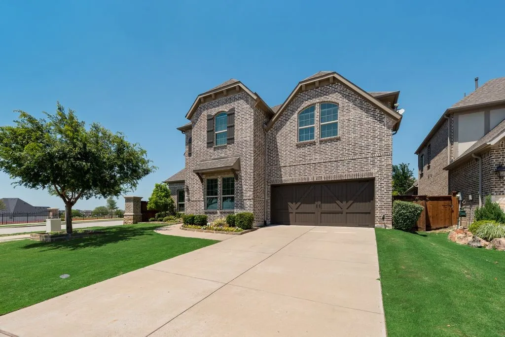 Brick exterior with dark shutters, attached two-car garage with arched windows, concrete driveway, and a manicured lawn