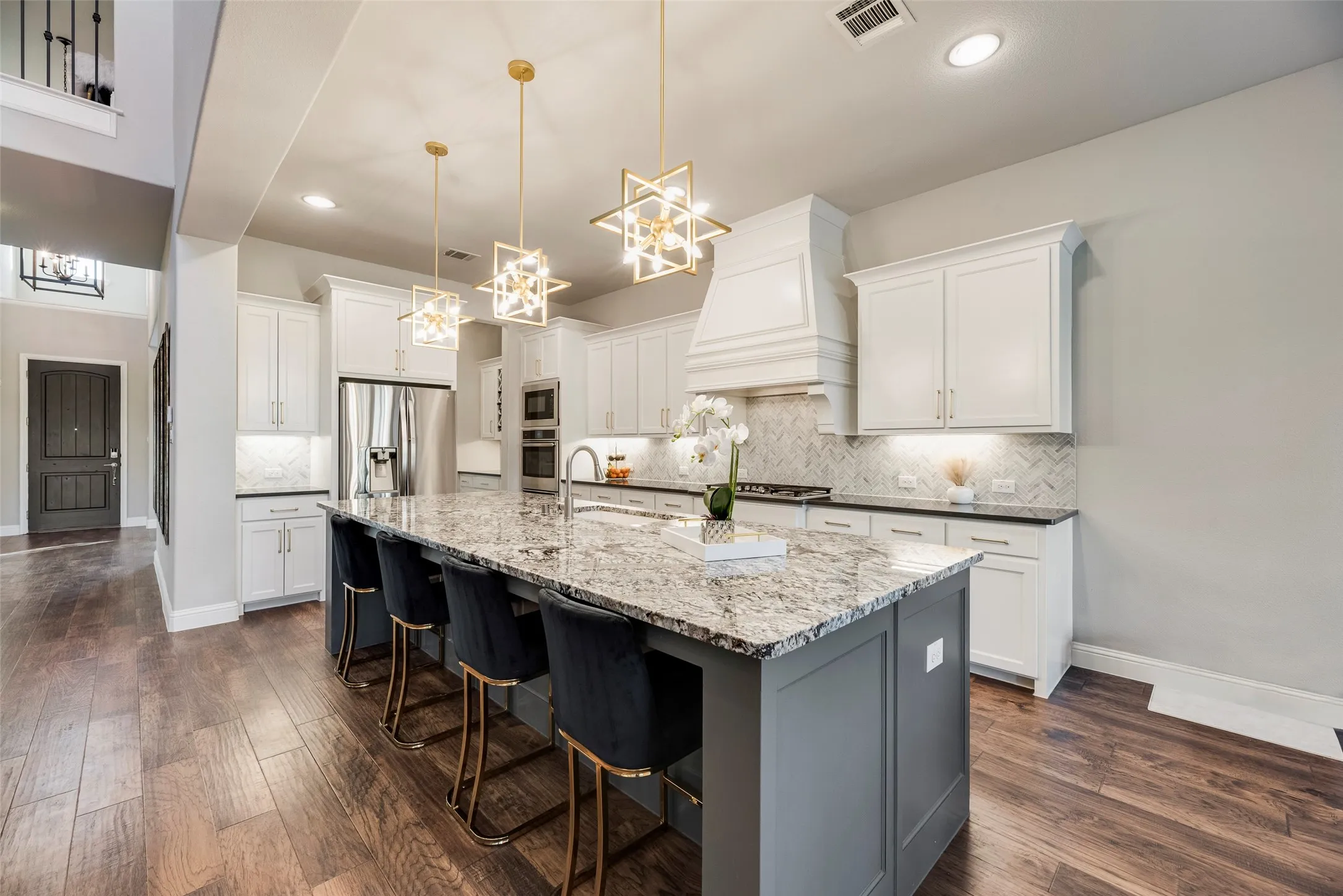 Spacious kitchen featuring an expansive center island with seating, pendant lighting, stainless steel appliances, white cabinetry, and wood-finish flooring