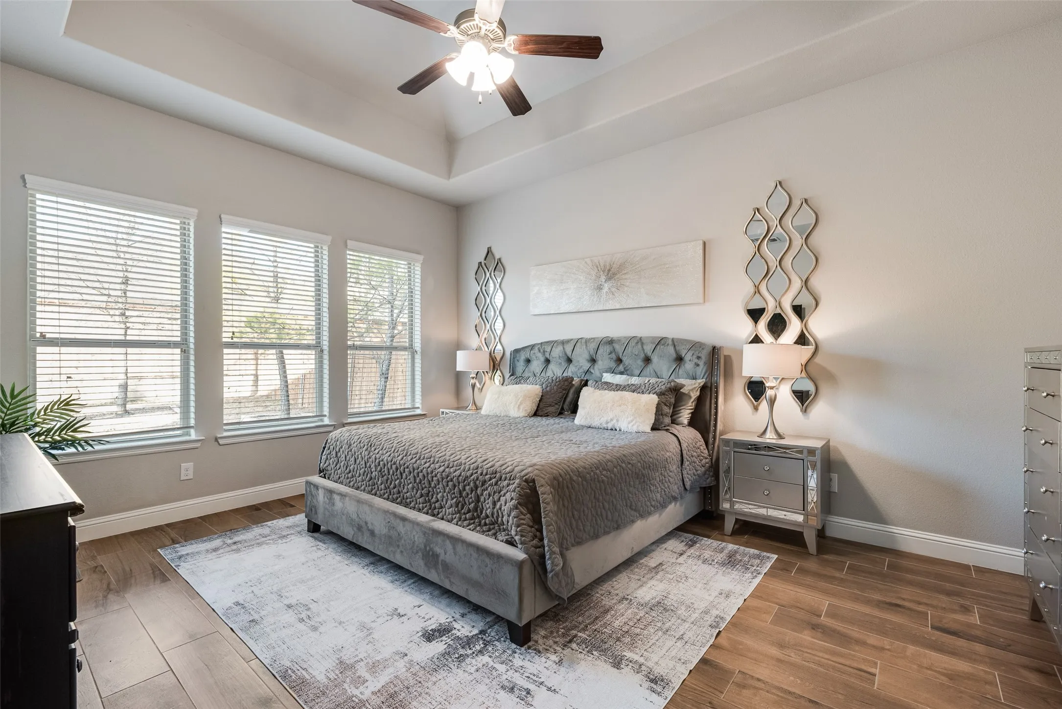 Tray ceiling with a ceiling fan, wood-finish flooring, and multiple windows