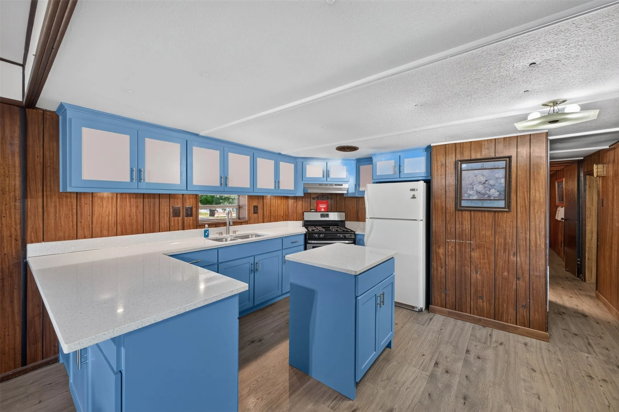 Kitchen featuring blue cabinetry, light-toned countertops, a stainless steel sink, and wood-finish flooring