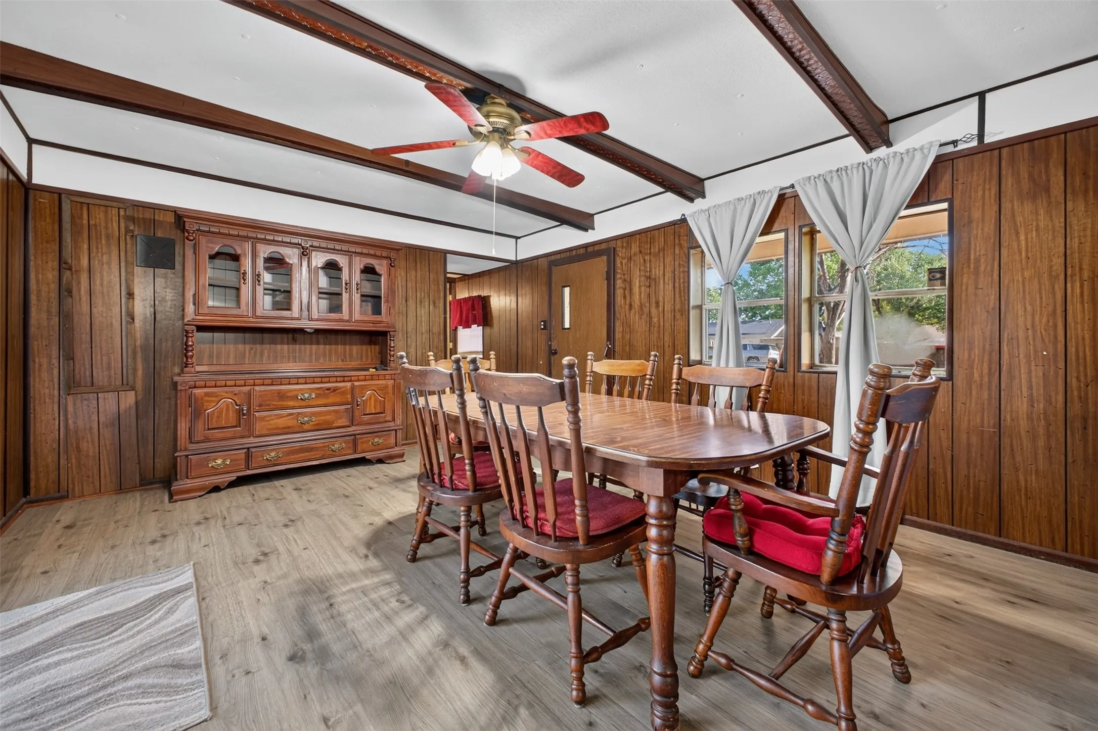 Wood-finish flooring, wood paneling, exposed ceiling beams, and a ceiling fan with integrated lighting