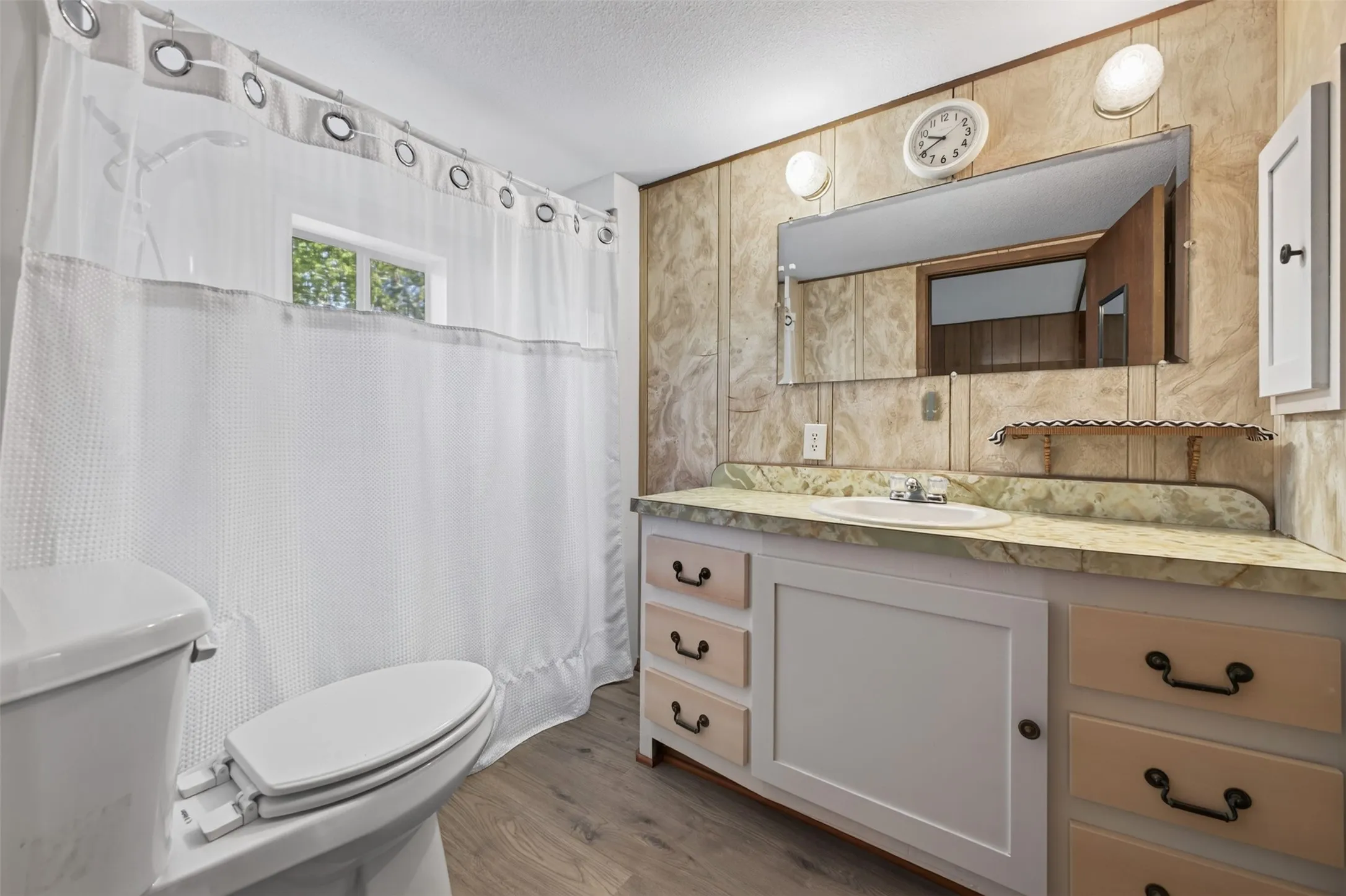 Vanity with integrated sink, wall-mounted mirror with sconce lighting, window, and wood-finish flooring