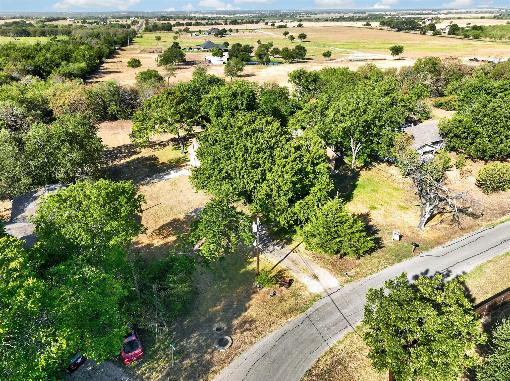 Expansive property featuring a winding road, mature trees, open fields, and distant structures