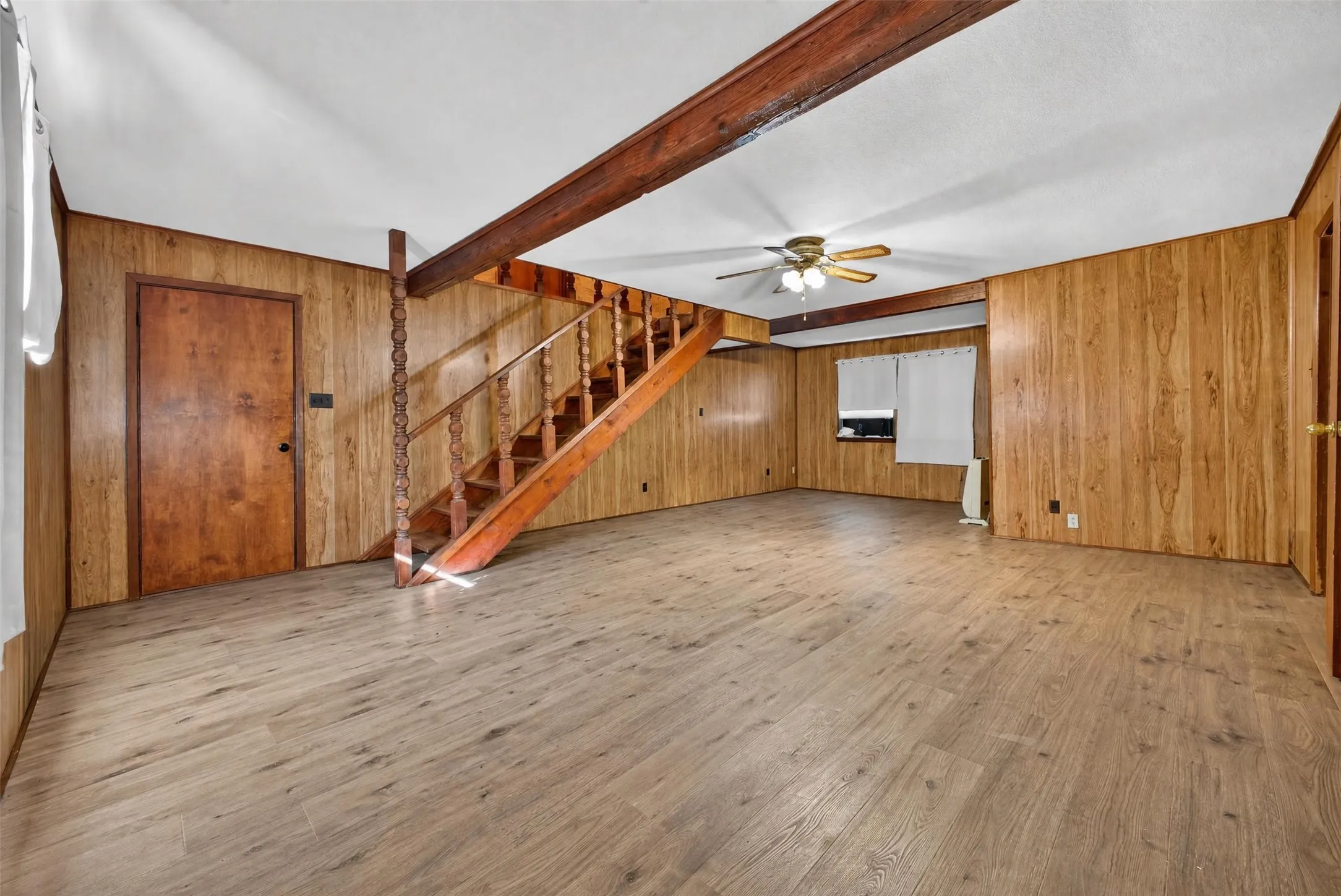 Wood-finish flooring with wood paneling walls, a wooden staircase, and a ceiling fan