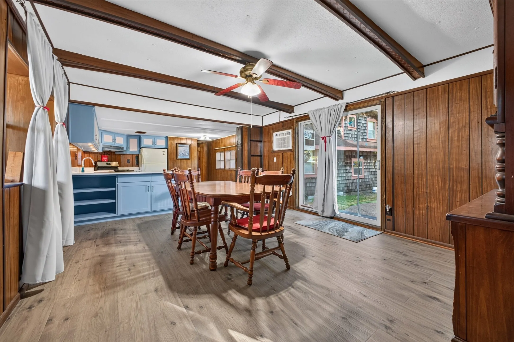 Wood-finish flooring throughout the dining area, exposed wood ceiling beams, and a sliding glass door to exterior