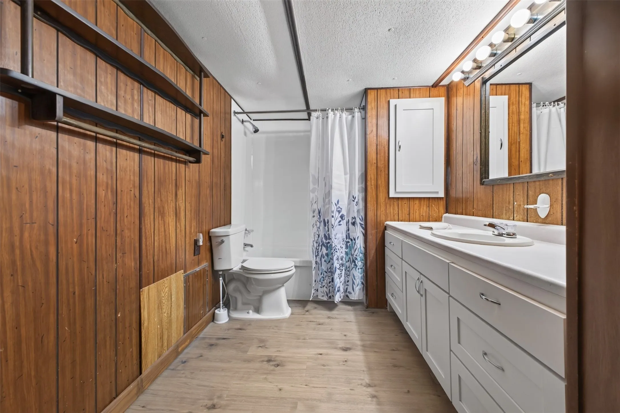 Wood-finish wall paneling, full vanity with integrated sink, built-in medicine cabinet, recessed bathtub, and wood-finish flooring