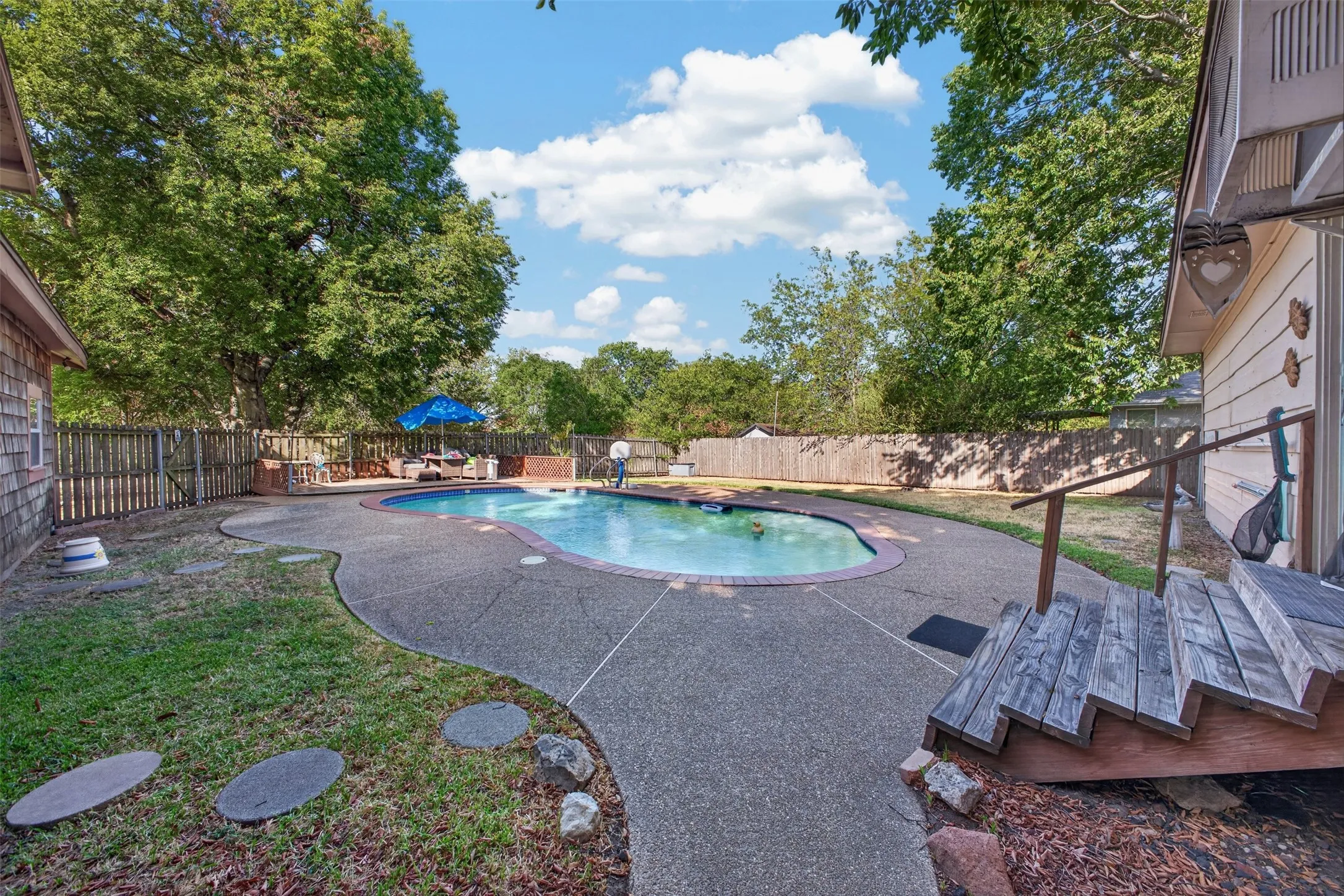 Backyard featuring a freeform swimming pool, concrete decking, and perimeter fencing