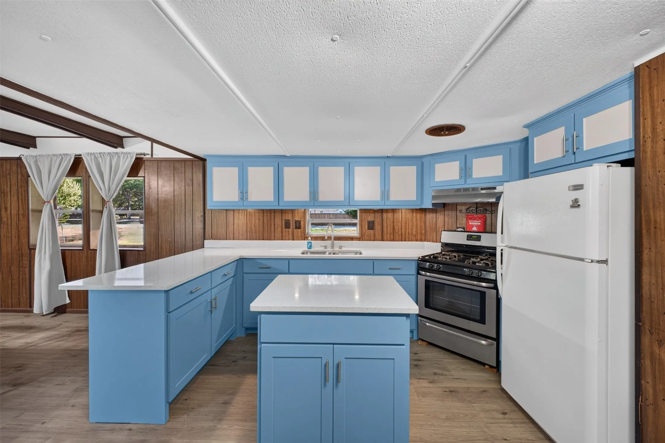 Kitchen featuring blue cabinetry, white countertops, stainless steel gas range, and wood-finish flooring