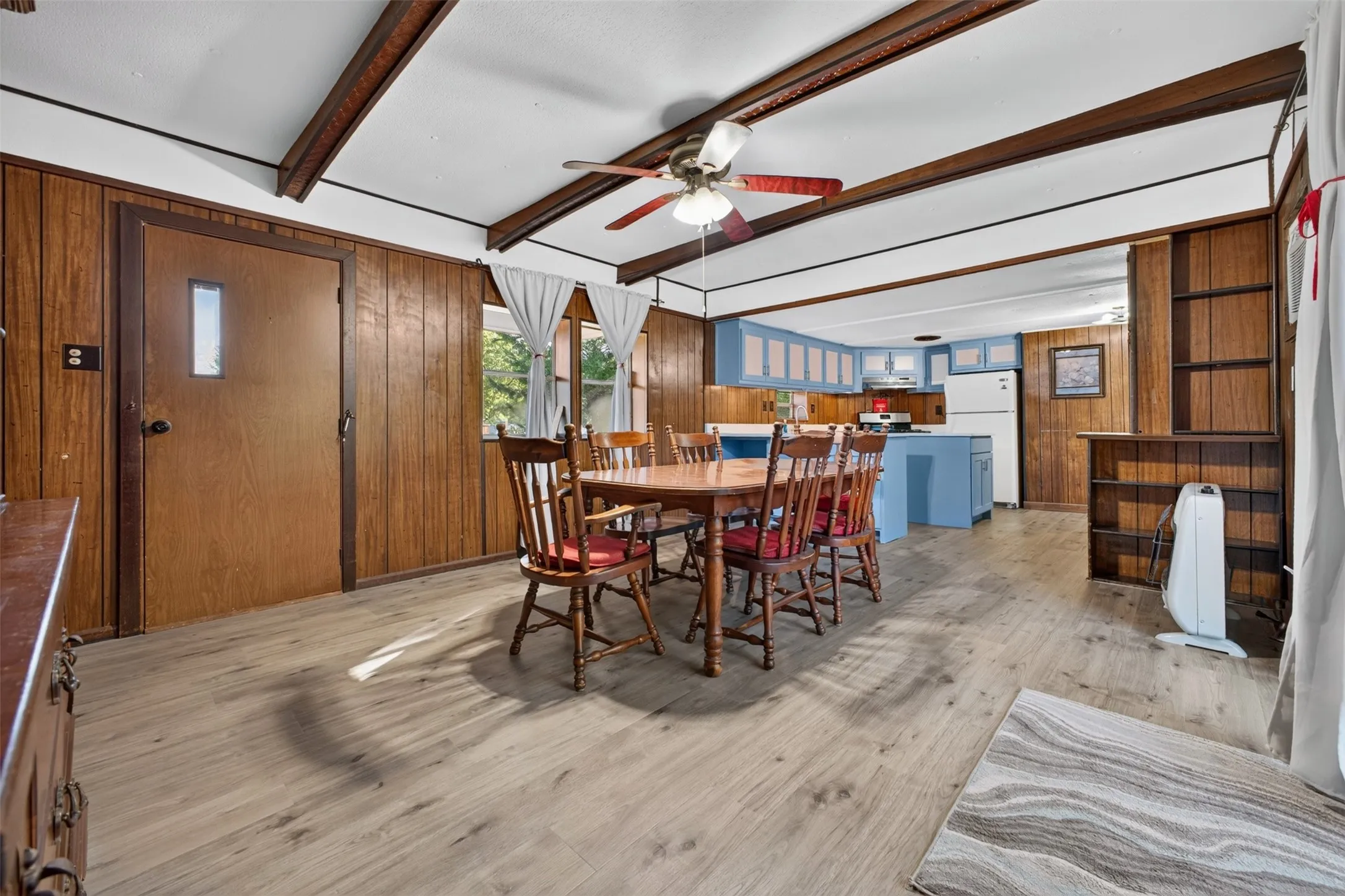 Wood-finish flooring throughout, exposed ceiling beams, wood paneling, and an open concept to the kitchen