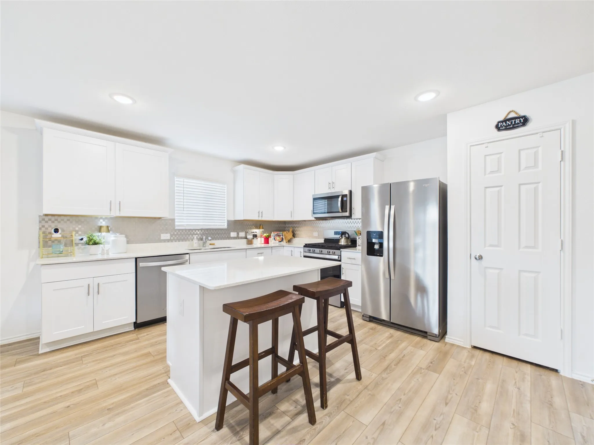 Open kitchen with granite countertops and modern backsplash with stainless steel appliance and island.