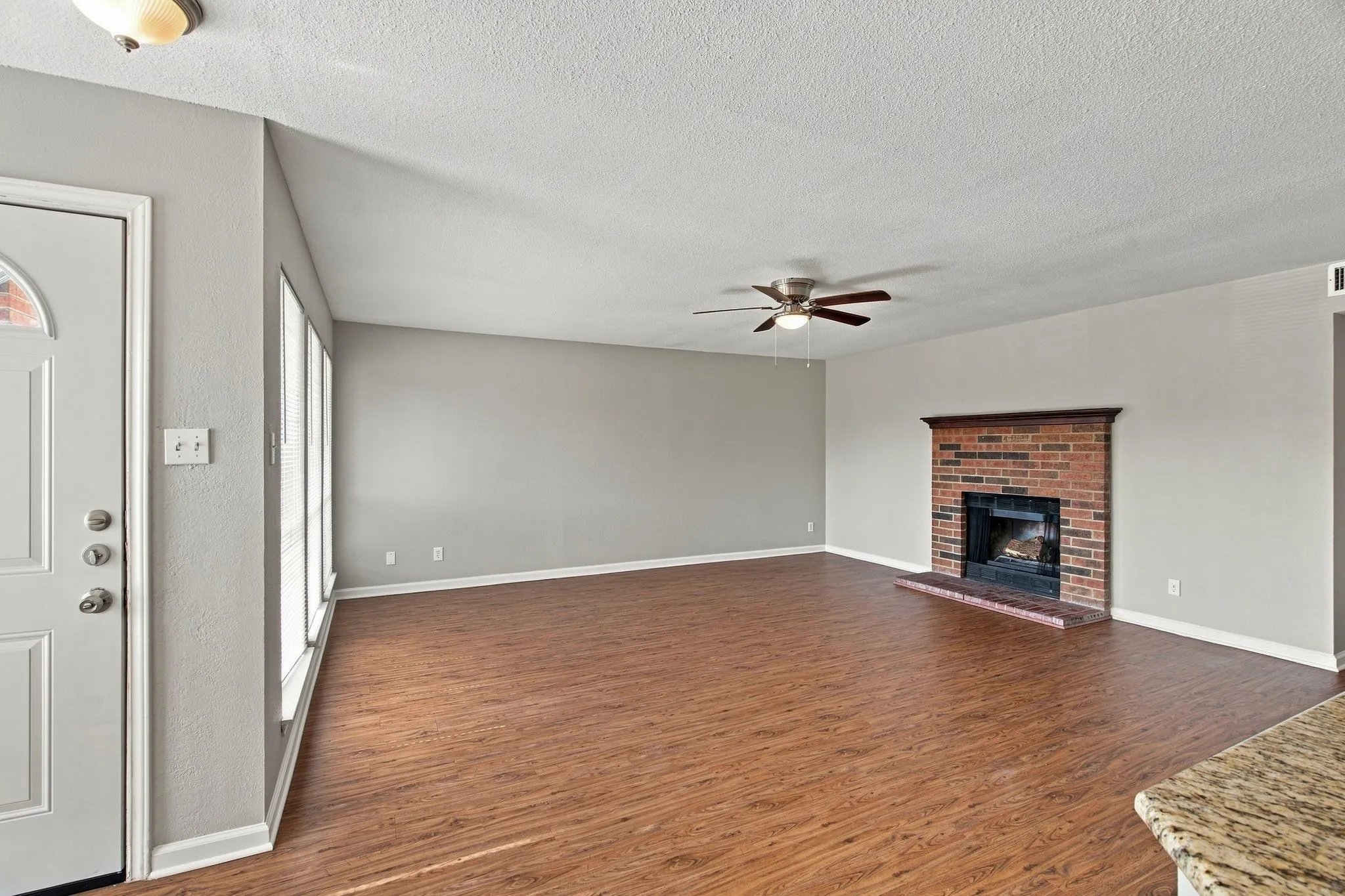 Unit D - Wood-finish flooring, brick fireplace with a wood mantle, ceiling fan, and multiple windows