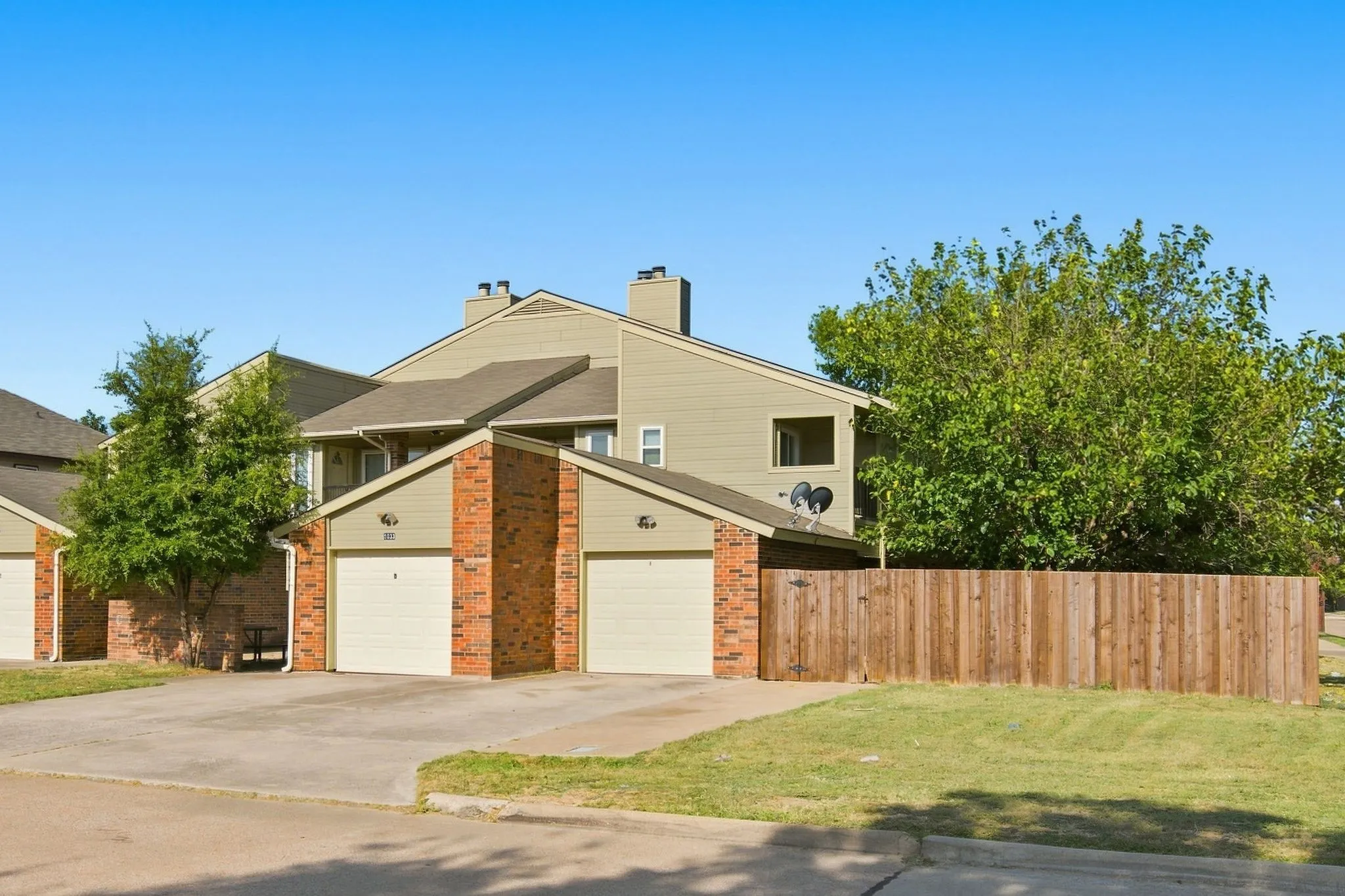 Multi-unit property featuring attached garages with beige doors, brick and siding exterior, and a wood privacy fence