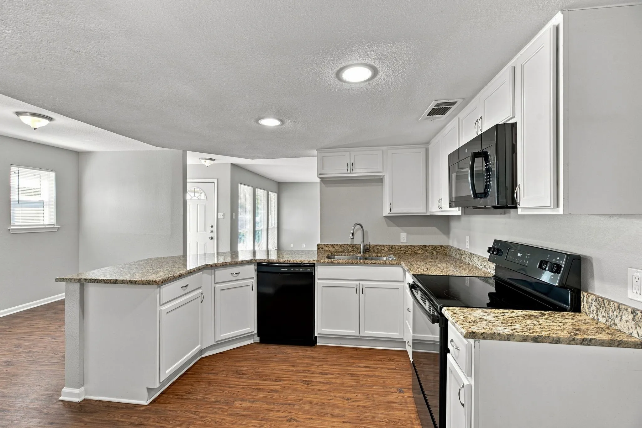 Unit D -Kitchen featuring wood-finish flooring, white cabinetry, spacious countertops, stainless steel sink, and black appliances