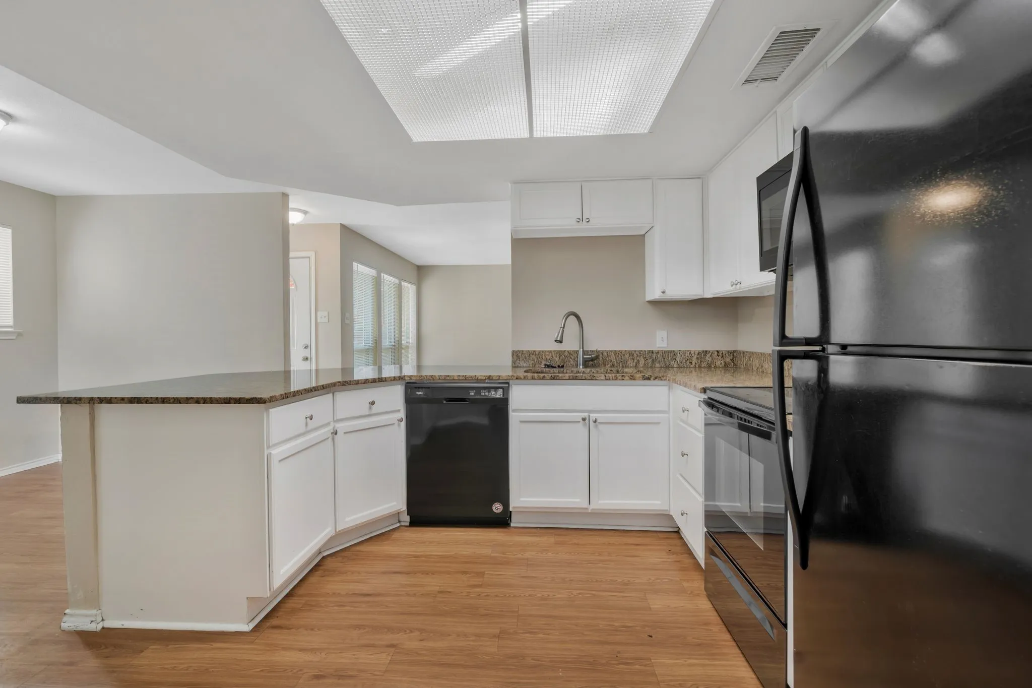 Unit B - -Kitchen featuring wood-finish flooring, white cabinetry, and integrated black appliances.