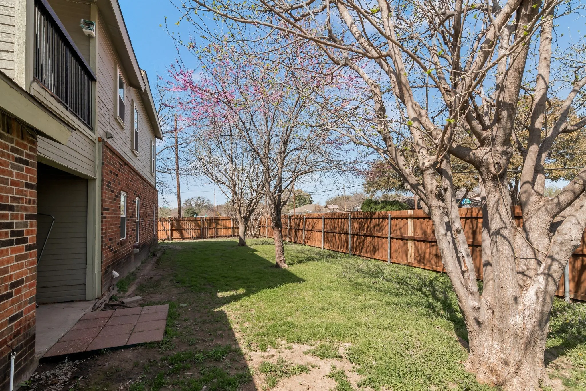 Unit B -Fenced backyard with mature trees, a red brick exterior, and a second-story balcony