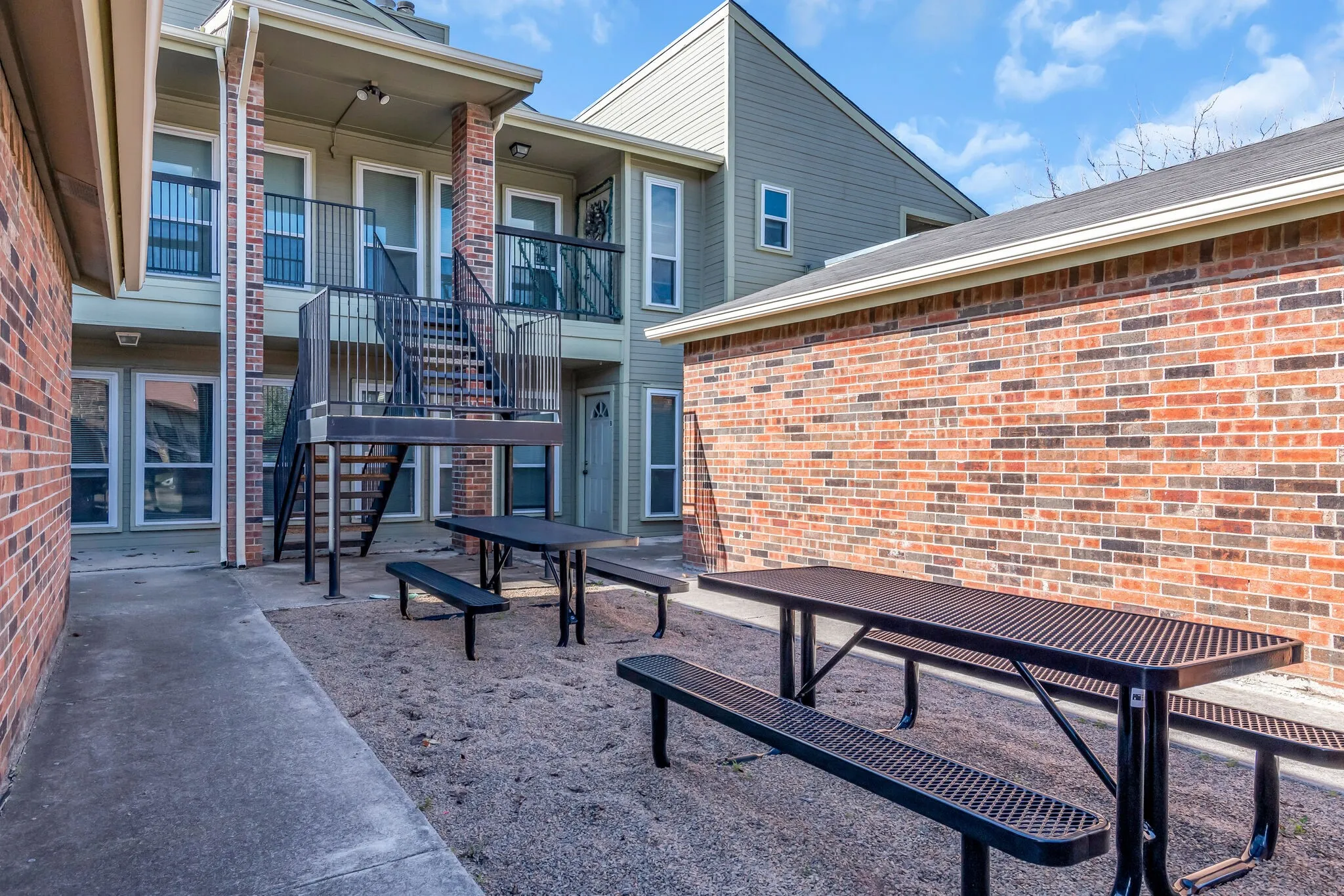 Unit A - Exterior brick facade with multiple private balconies, metal stairwell access, and ground-level patios