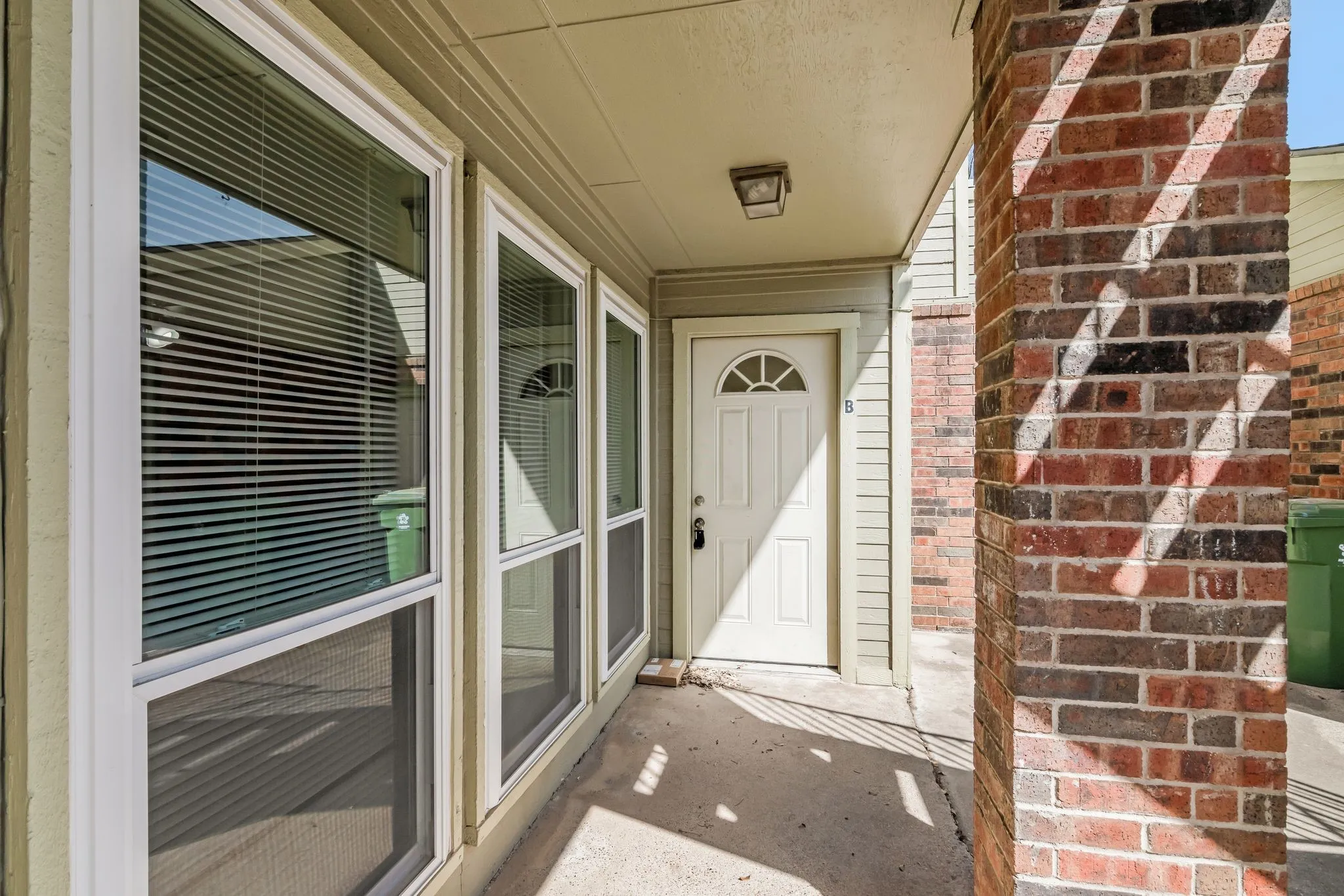 Unit B - Entryway featuring a white paneled door with an arched lite, brick accent column, and multiple vertical windows