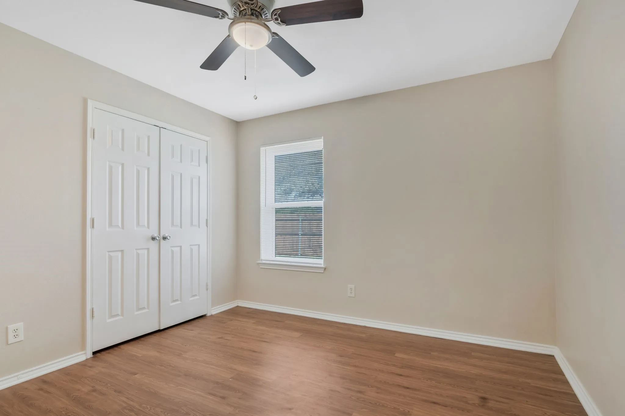 Unit B -Wood-finish flooring with light-toned walls, a ceiling fan with integrated lighting, a window, and bifold paneled doors