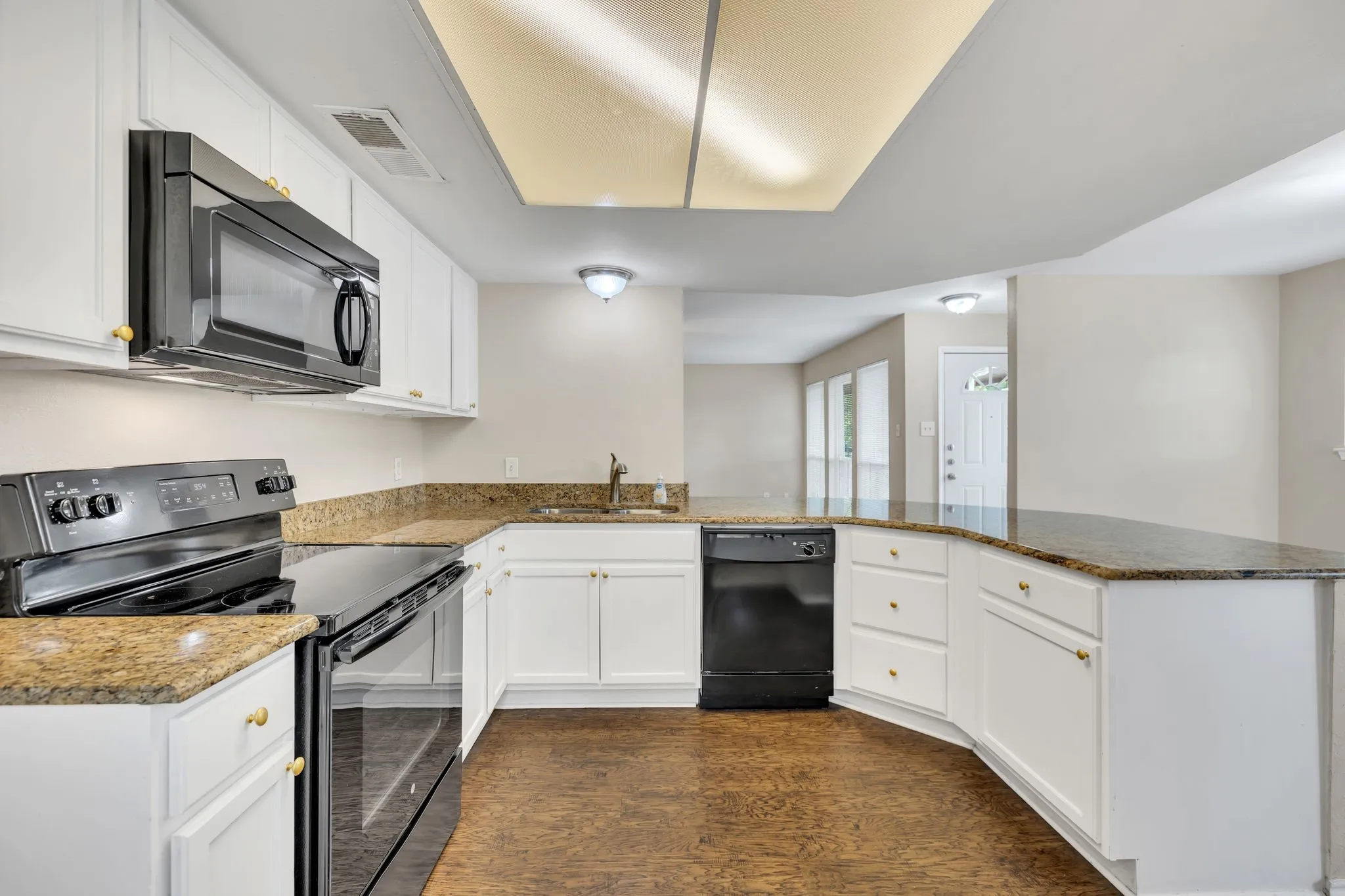 Unit C- Kitchen featuring white cabinetry, granite-style countertops, integrated black appliances, and durable flooring