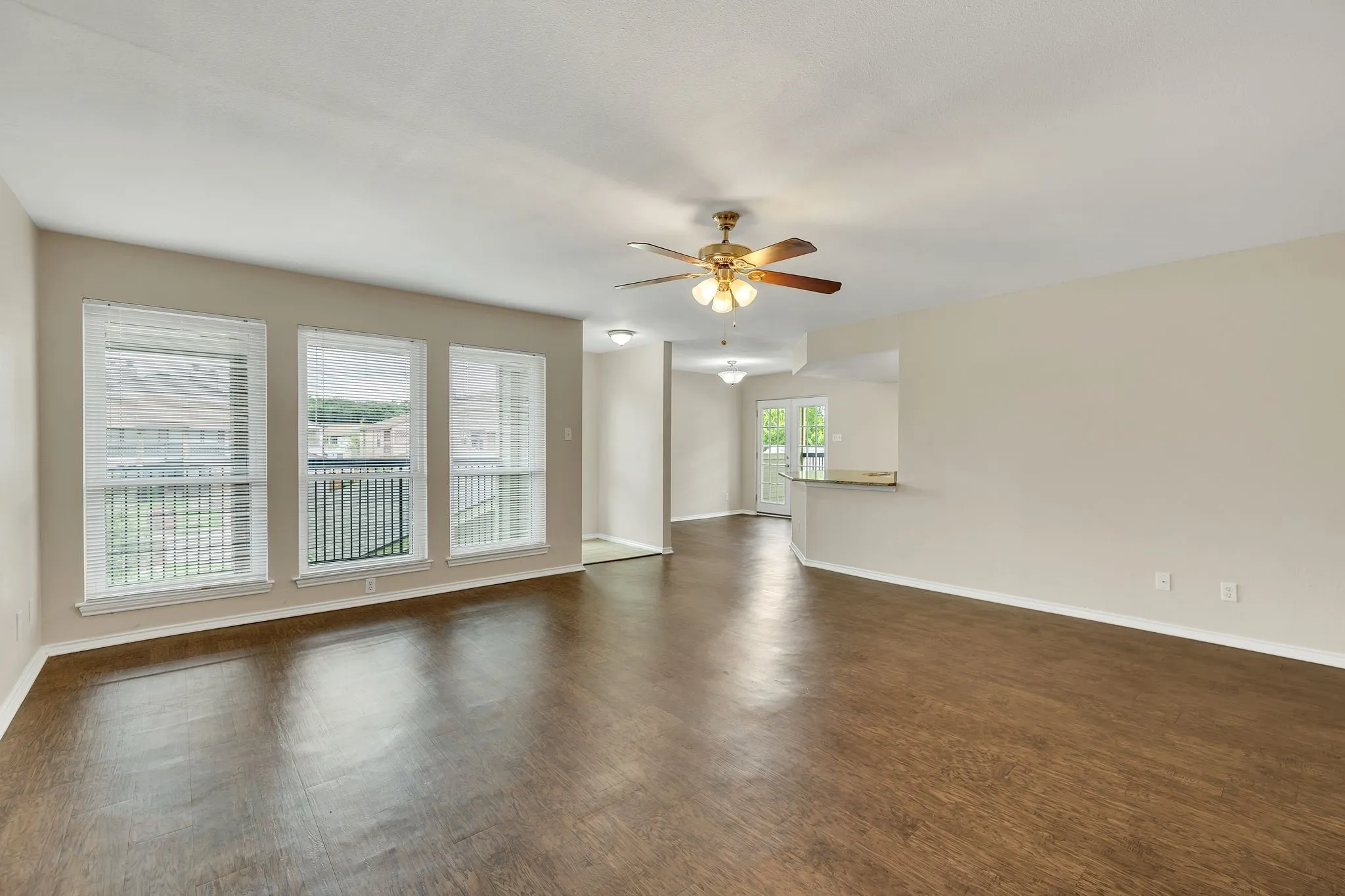 Unit C- Spacious living area featuring wood-finish flooring, ample natural light from multiple windows, and a ceiling fan with integrated lighting