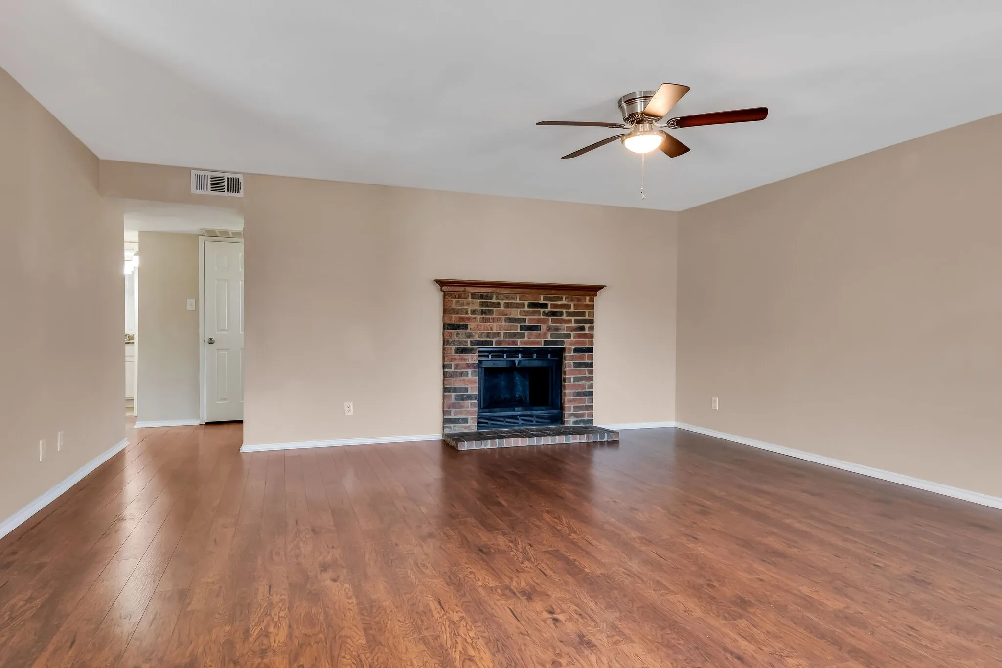 Unit A - Wood-finish flooring throughout, brick fireplace with wood mantel, and a ceiling fan with integrated lighting