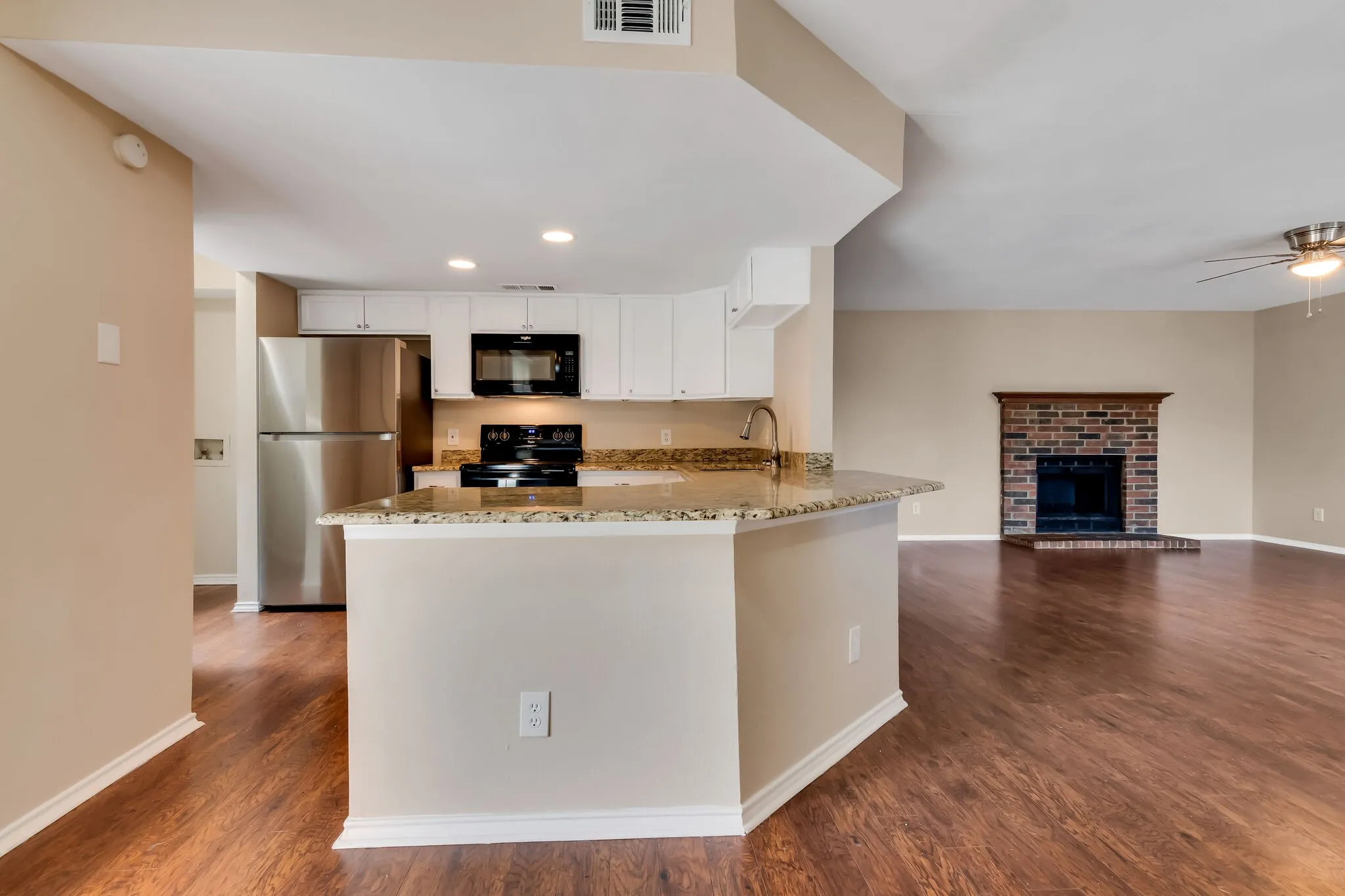 Unit A - Kitchen featuring white cabinetry, stainless steel refrigerator, black microwave, and granite countertops with a breakfast bar