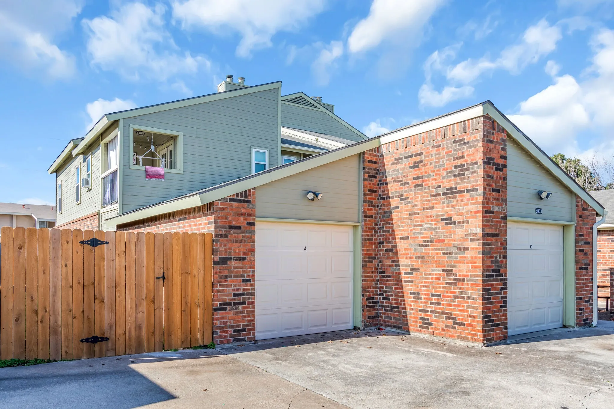 Brick and siding exterior with pitched roofs, two garage doors, and a wood privacy fence
