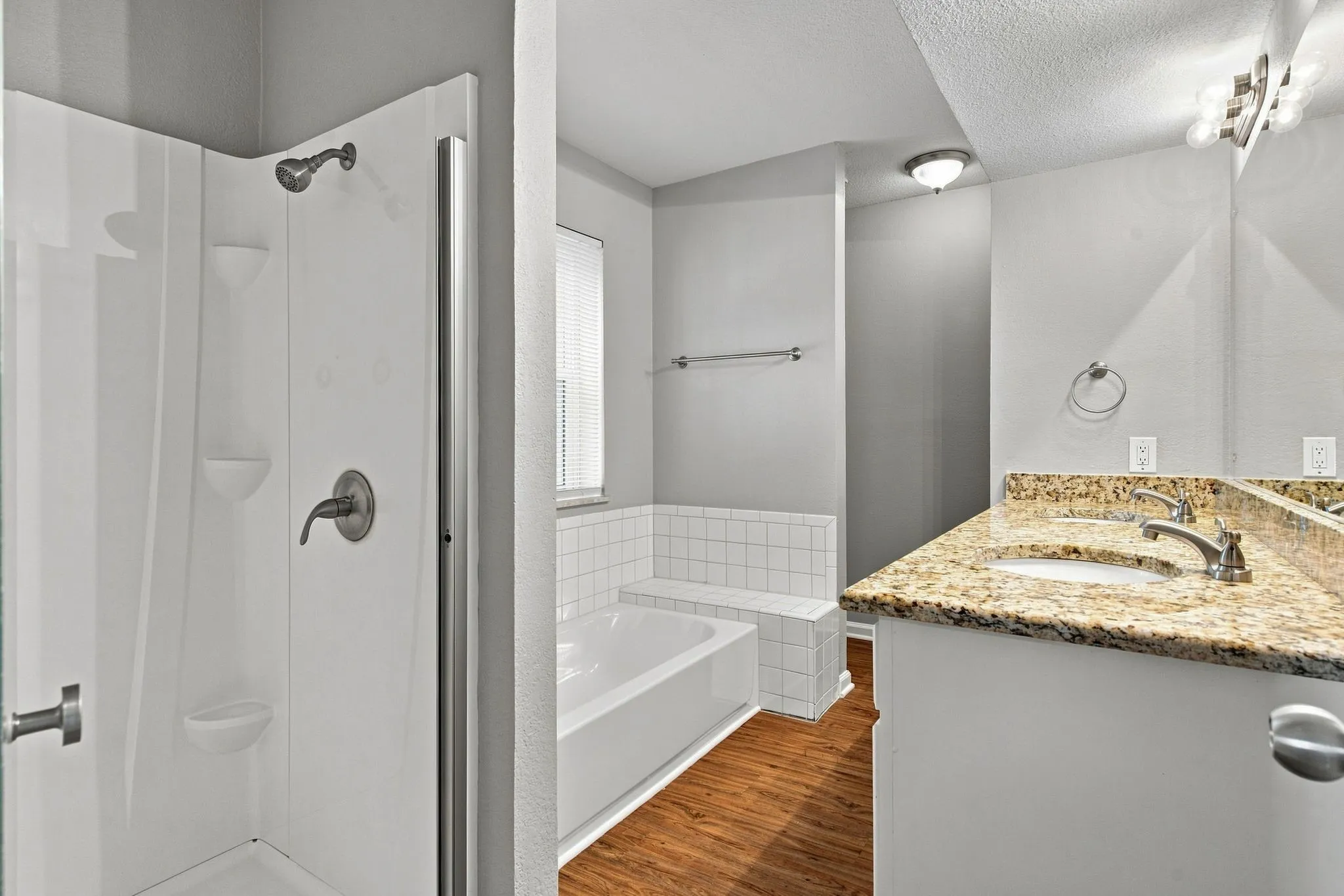 Unit D -Double vanity with stone countertop, wood-finish flooring, built-in bathtub, and separate shower with brushed nickel fixtures
