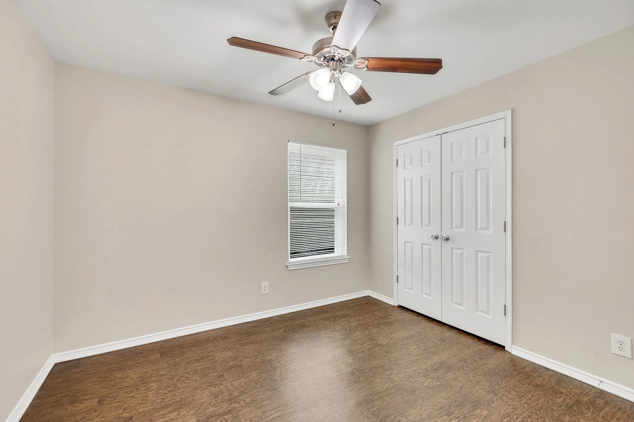 Unit C- Wood-finish flooring with white trim, ceiling fan with light fixture, window with blinds, and paneled double closet doors