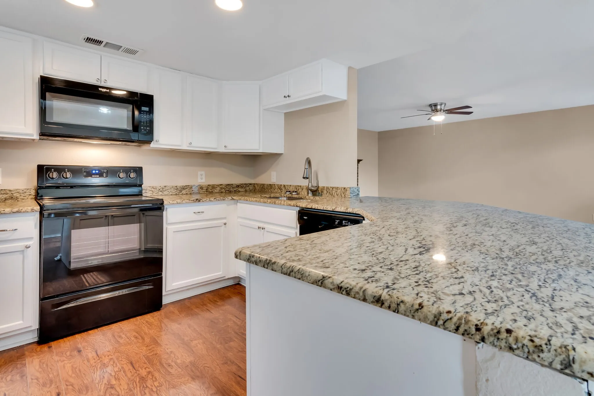 Unit A - White cabinetry, granite countertops, black kitchen appliances, wood-finish flooring, and a ceiling fan