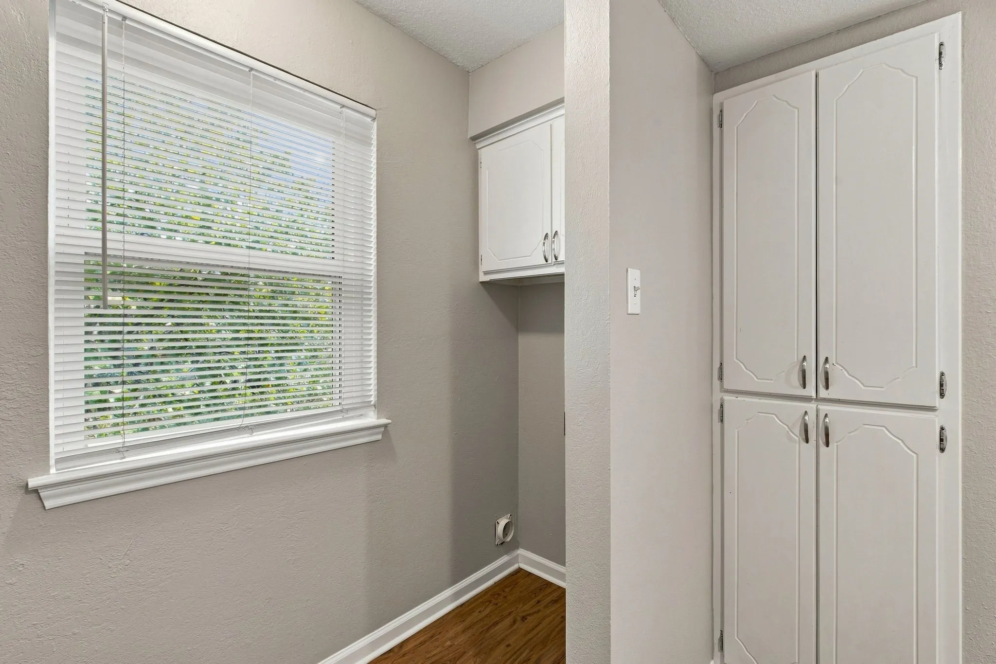 Unit D - Recessed window with white blinds, wood-finish flooring, white built-in cabinetry, and white wall cabinets