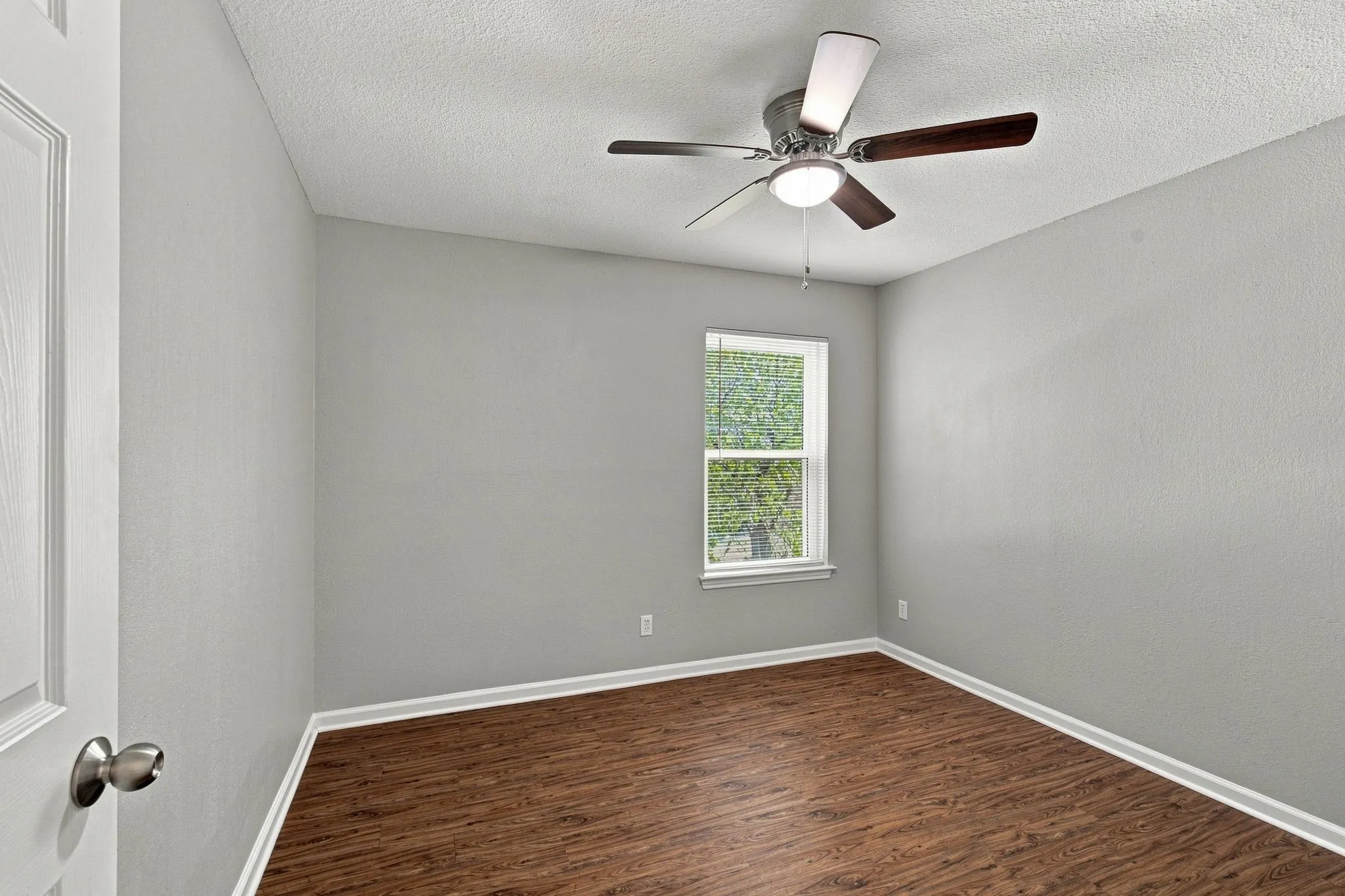 Unit D -Wood-finish flooring, ceiling fan with integrated lighting, single window, and white trim accents