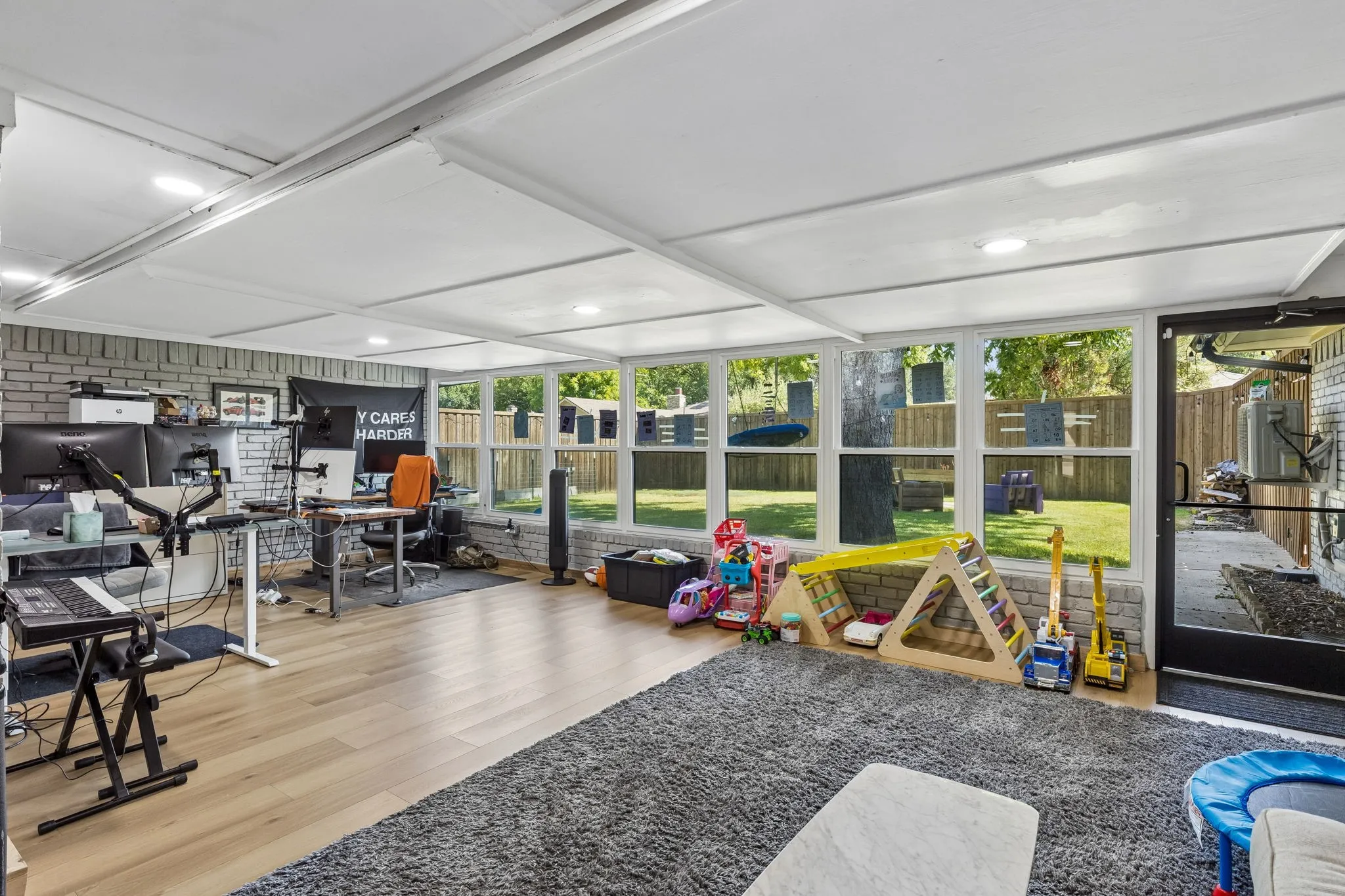 Floor-to-ceiling windows, light wood-finish flooring, recessed lighting, and white exposed brick wall