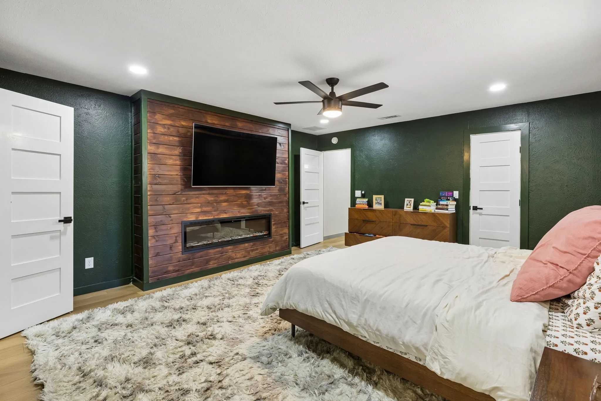 Wood-finish accent wall with integrated linear fireplace, recessed lighting, and a ceiling fan