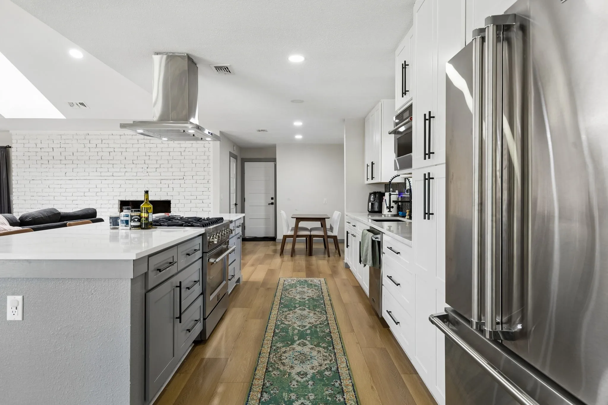Kitchen featuring a large center island, built-in stainless steel appliances, white cabinetry with dark hardware, and wood-finish flooring