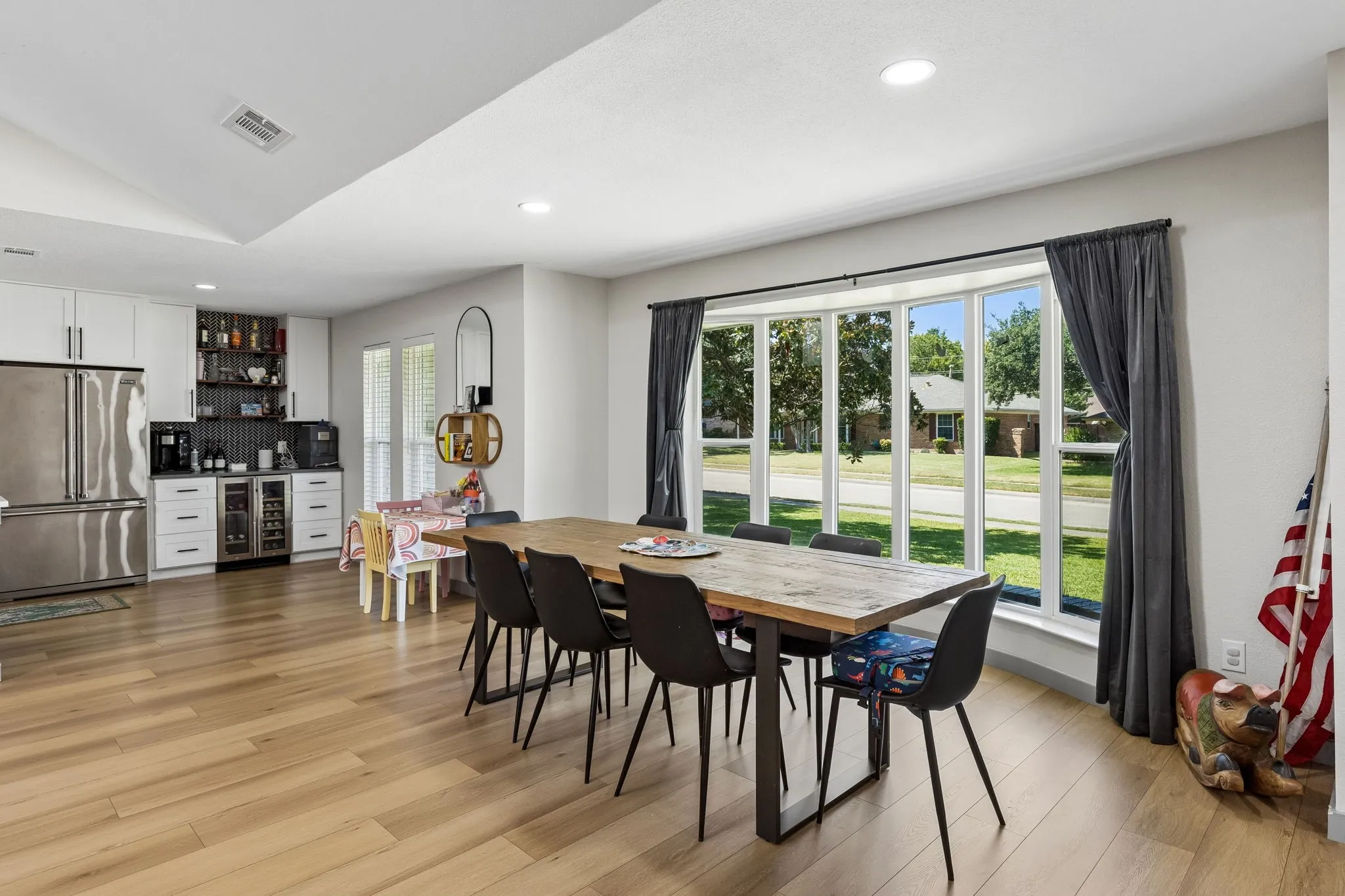 Wood-finish flooring throughout, bay window with multiple panes, recessed ceiling lighting, built-in beverage refrigerator, and white cabinetry with dark hardware
