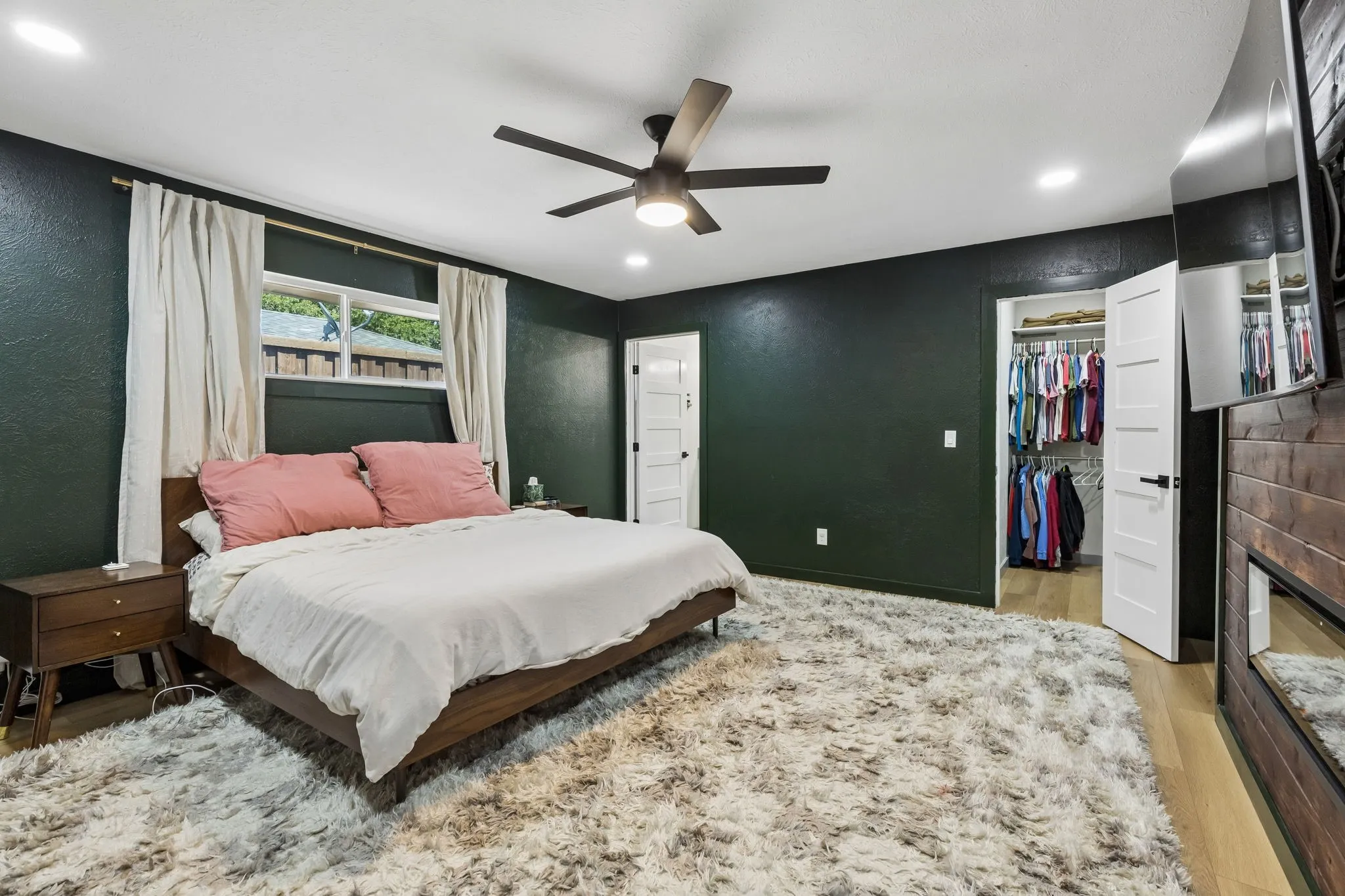 Recessed lighting, ceiling fan, wood-finish flooring, white paneled door, and a built-in wall unit with a mounted television