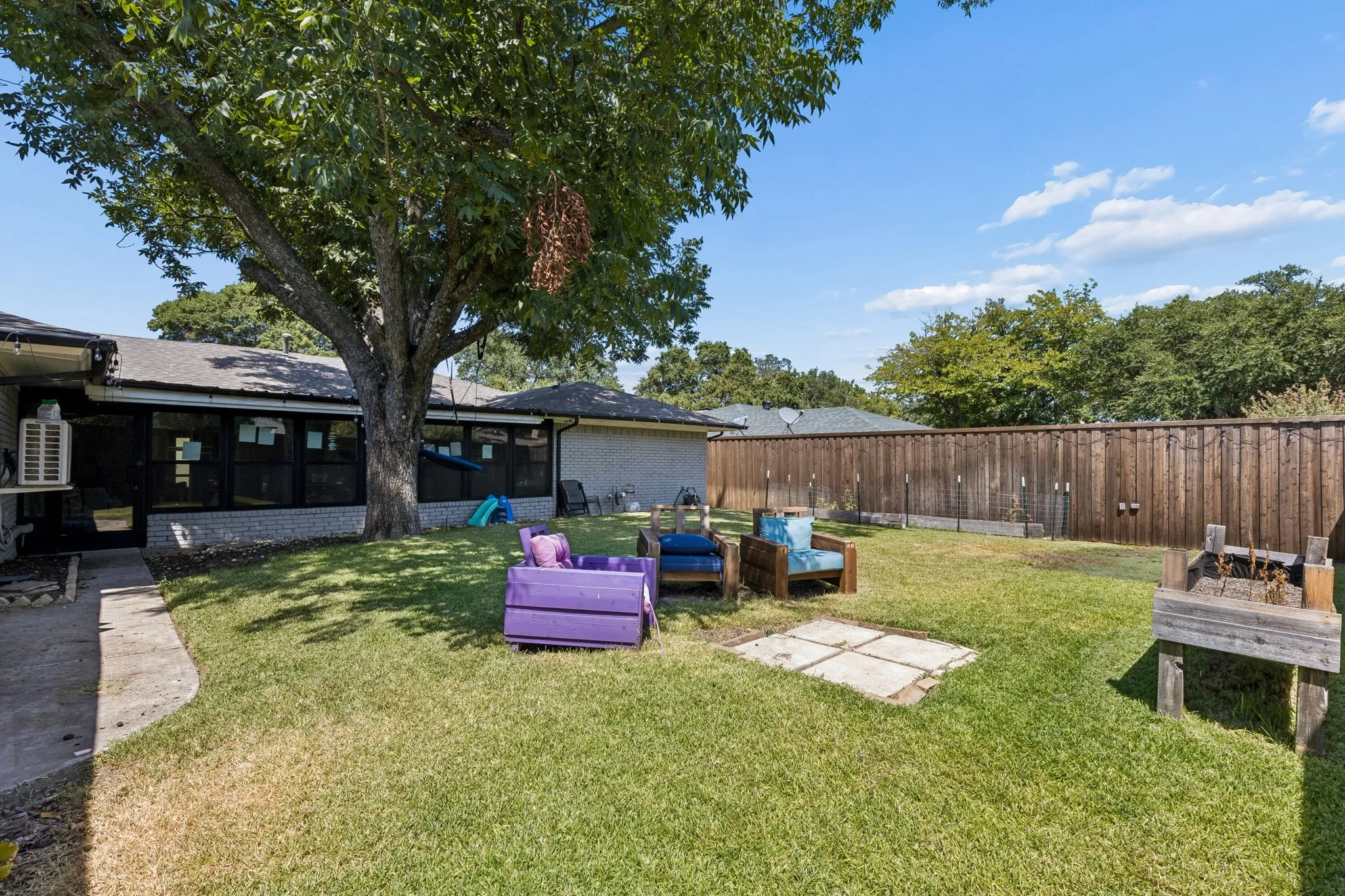 Expansive backyard oasis featuring a mature shade tree, manicured lawn, wooden privacy fencing, and multiple entertaining spaces including built-in seating areas and a detached storage structure