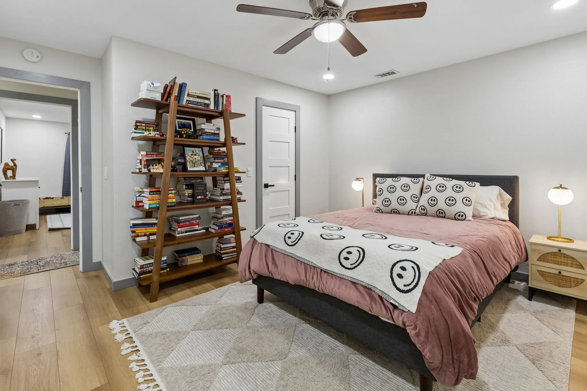 Recessed lighting, ceiling fan with wood-finish blades, wood-finish flooring, white paneled door with black hardware, and an additional room entrance with grey trim