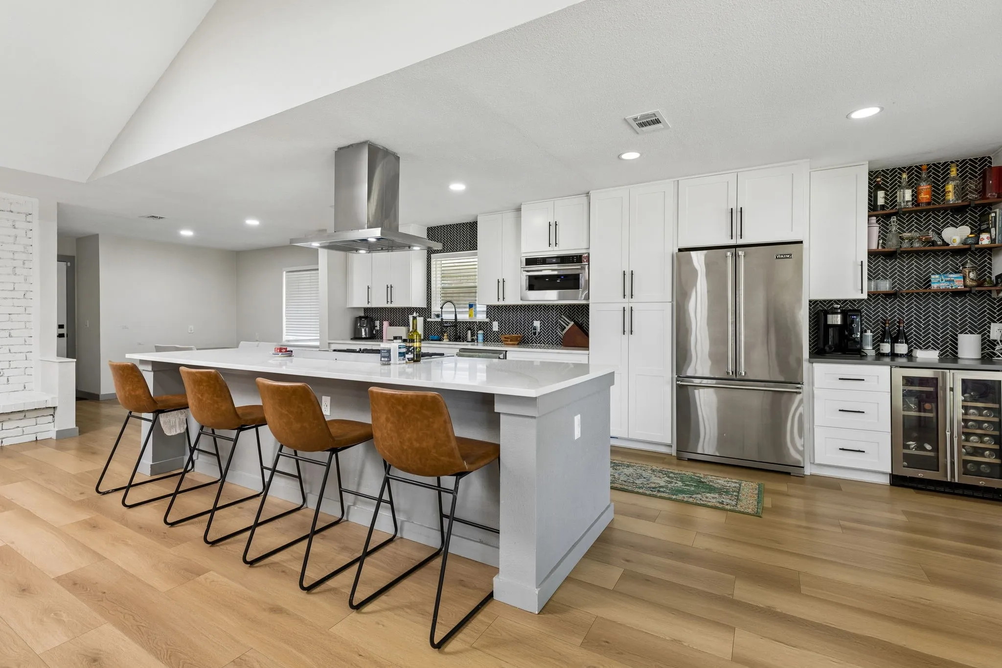 Contemporary kitchen with wood-finish flooring, a large center island, white cabinetry, stainless steel appliances, and recessed lighting