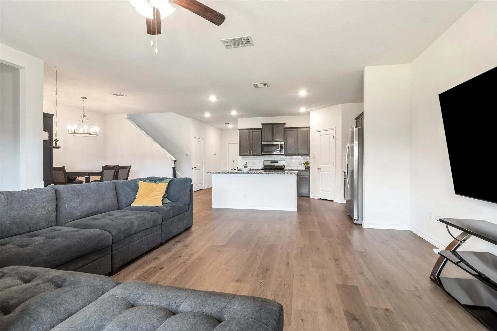 Open-concept main living area featuring wood-finish flooring, recessed lighting, a modern ceiling fan, and a kitchen island with a light-toned countertop