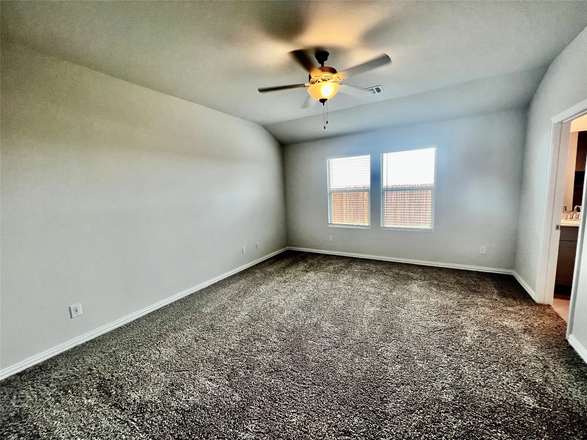 Spacious room featuring textured carpeting, neutral wall finishes, and a ceiling fan with integrated lighting