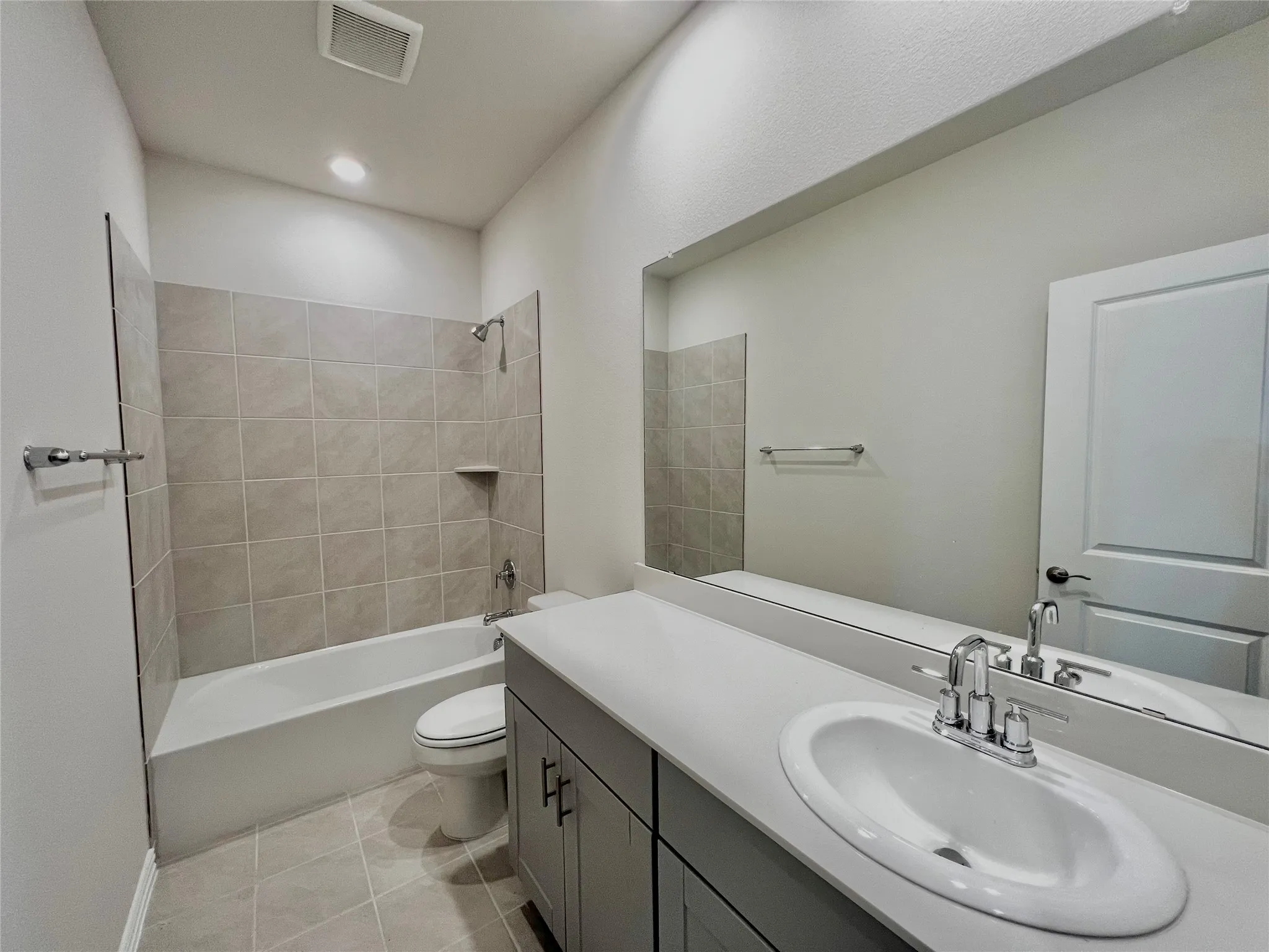 Full-size mirror, integrated vanity sink, two-door vanity cabinet, bathtub with shower fixture, and tiled shower surround